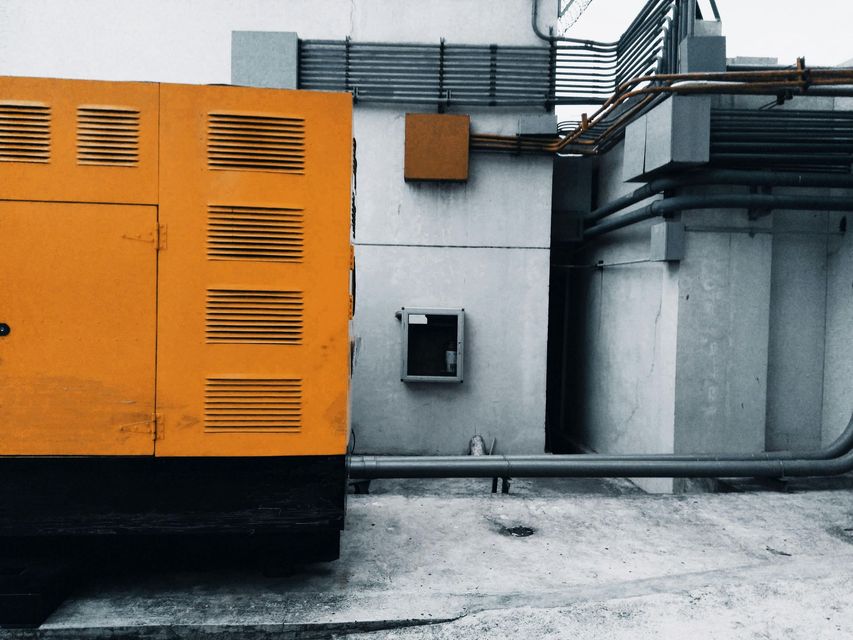 Orange industrial machine beside gray rooftop equipment and ducts on a concrete surface