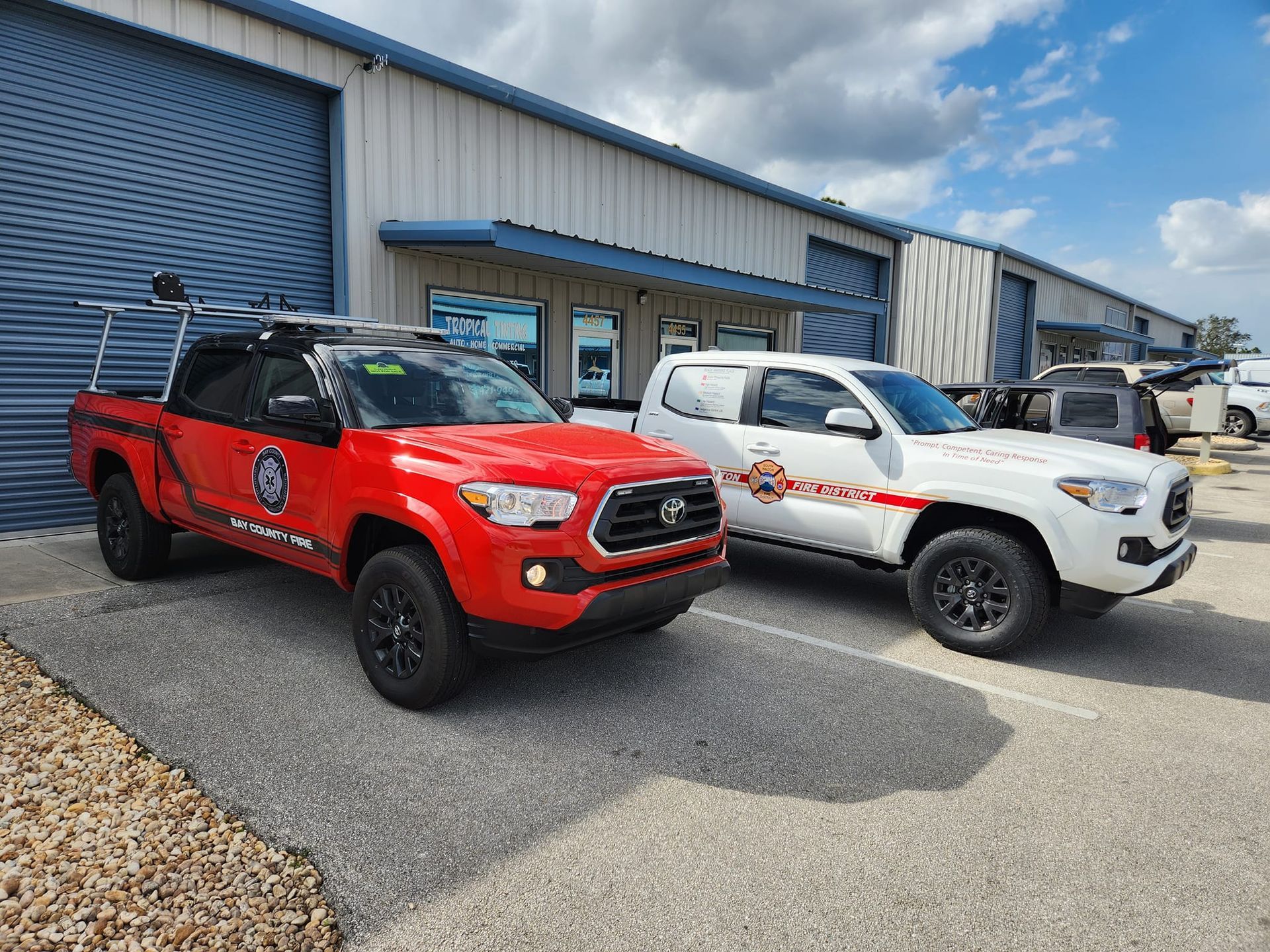 Two red and white trucks are parked in front of a building.