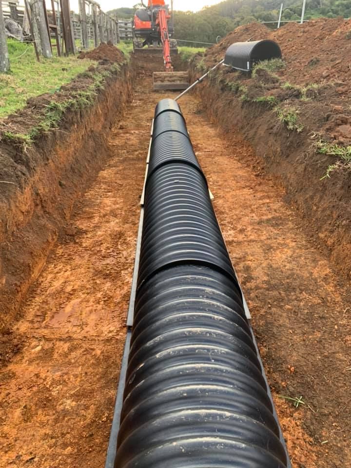 A large black pipe is being installed in a trench — Matt King Plumbing & Septic Systems in Nabiac, NSW