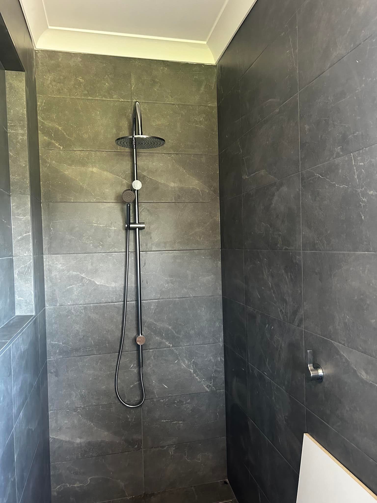 A shower with a black tile wall and a shower head — Matt King Plumbing & Septic Systems in Old Bar, NSW