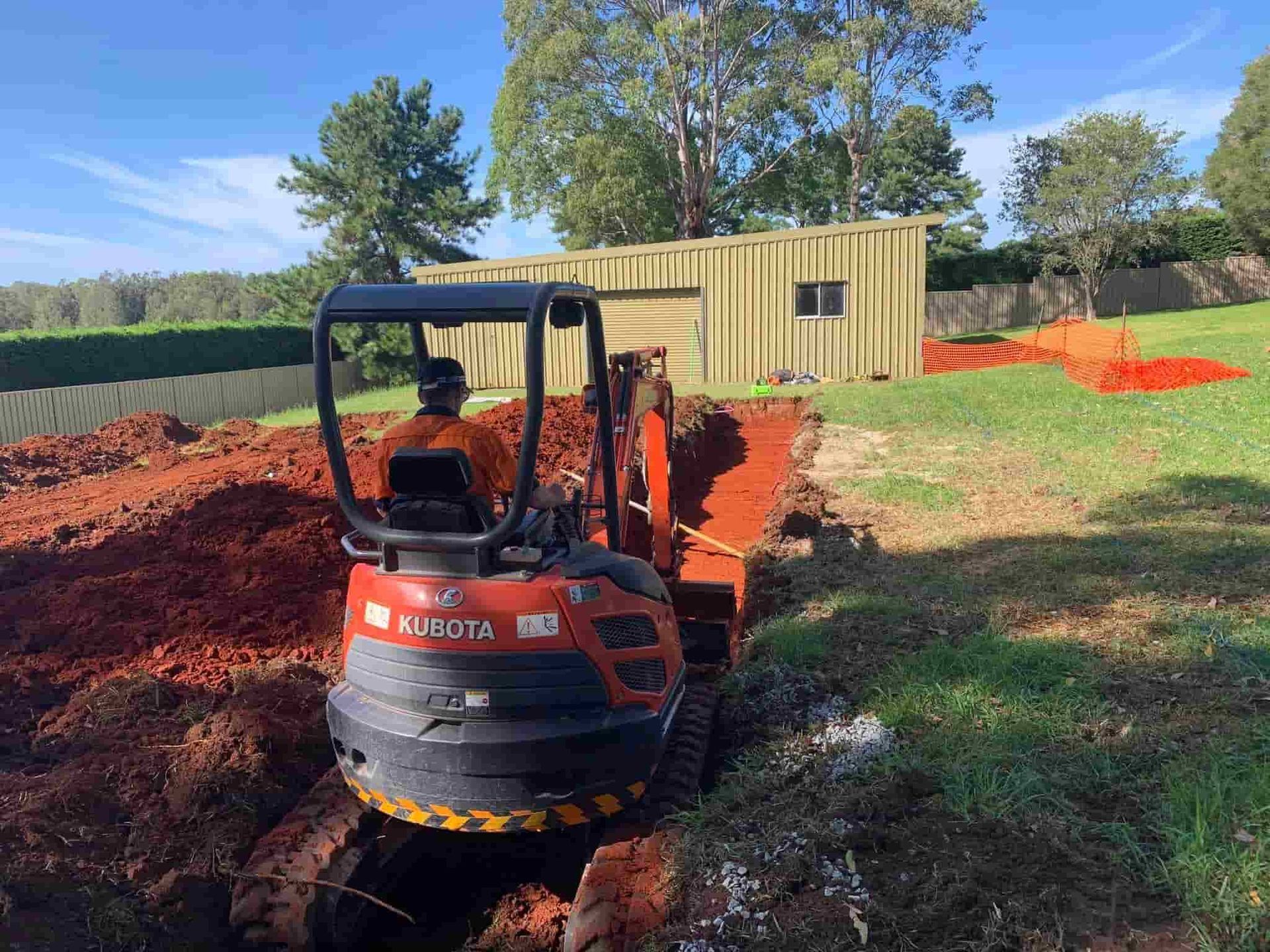 A Man Is Driving a Small Excavator in A Dirt Field — Matt King Plumbing & Septic Systems in Wauchope, NSW