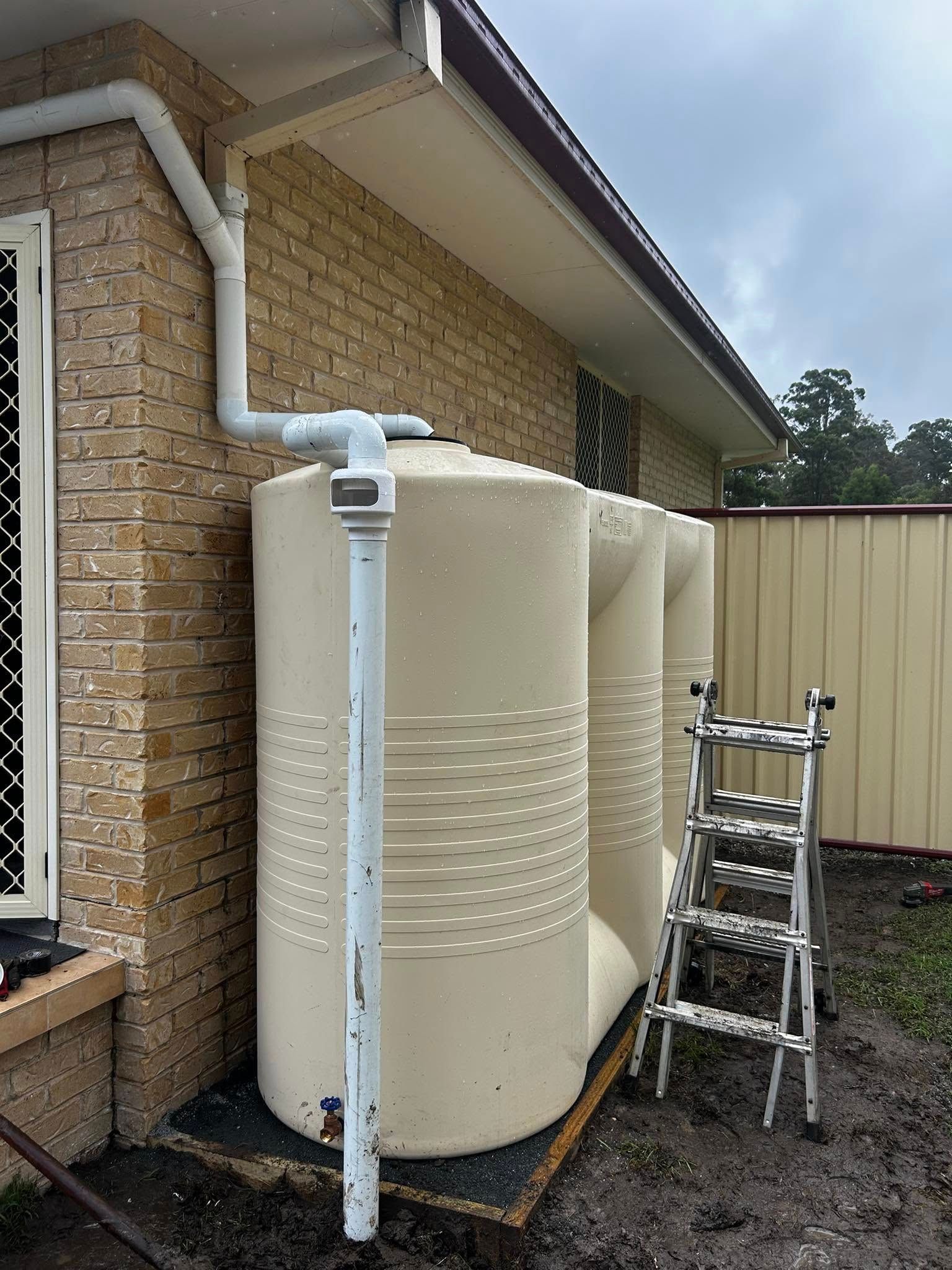 A watertank with a downpipe in front of a brick house — Matt King Plumbing & Septic Systems in Taree, NSW