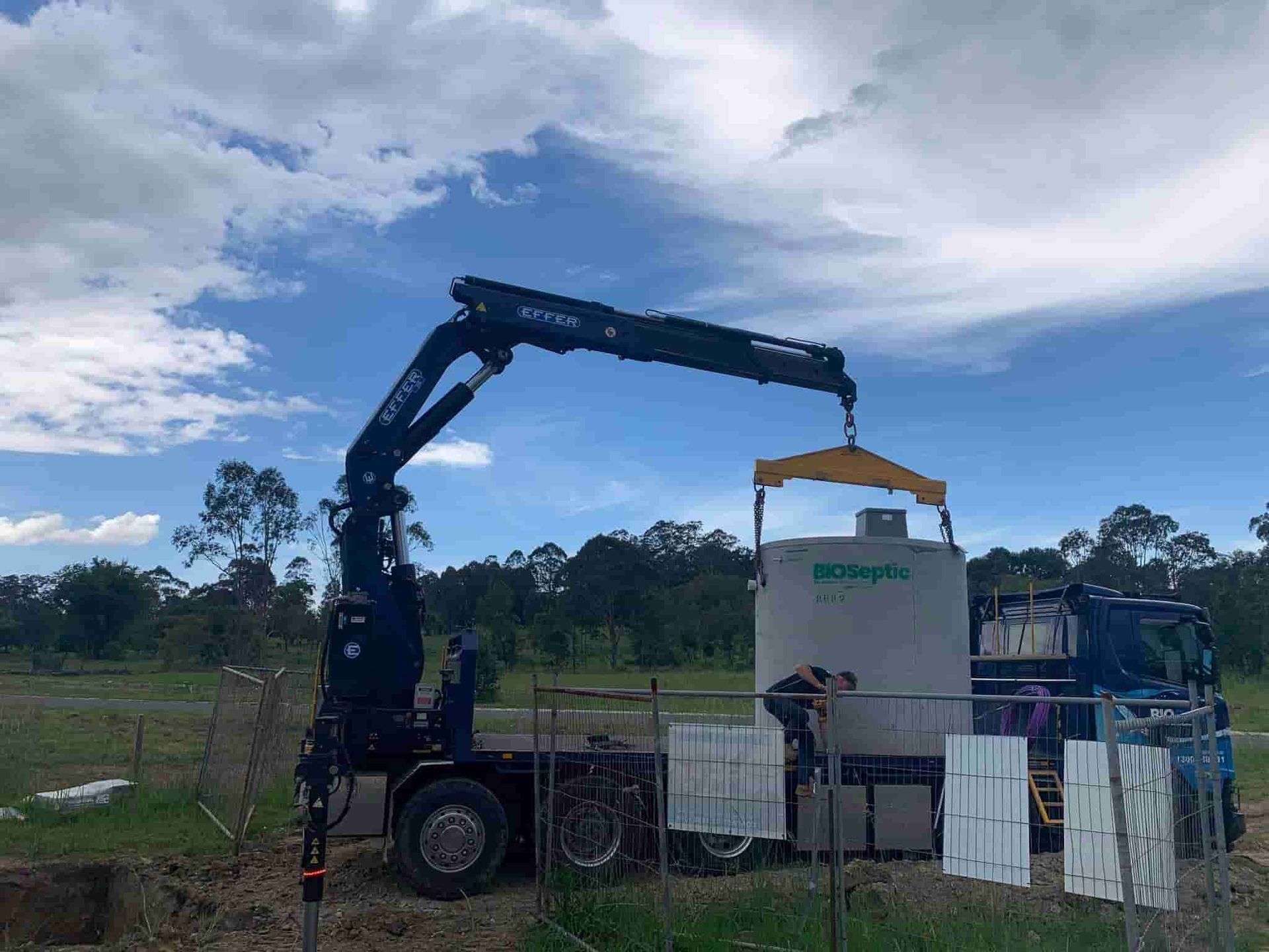 A Crane Is Lifting a Large Concrete Block from A Truck — Matt King Plumbing & Septic Systems in Taree, NSW