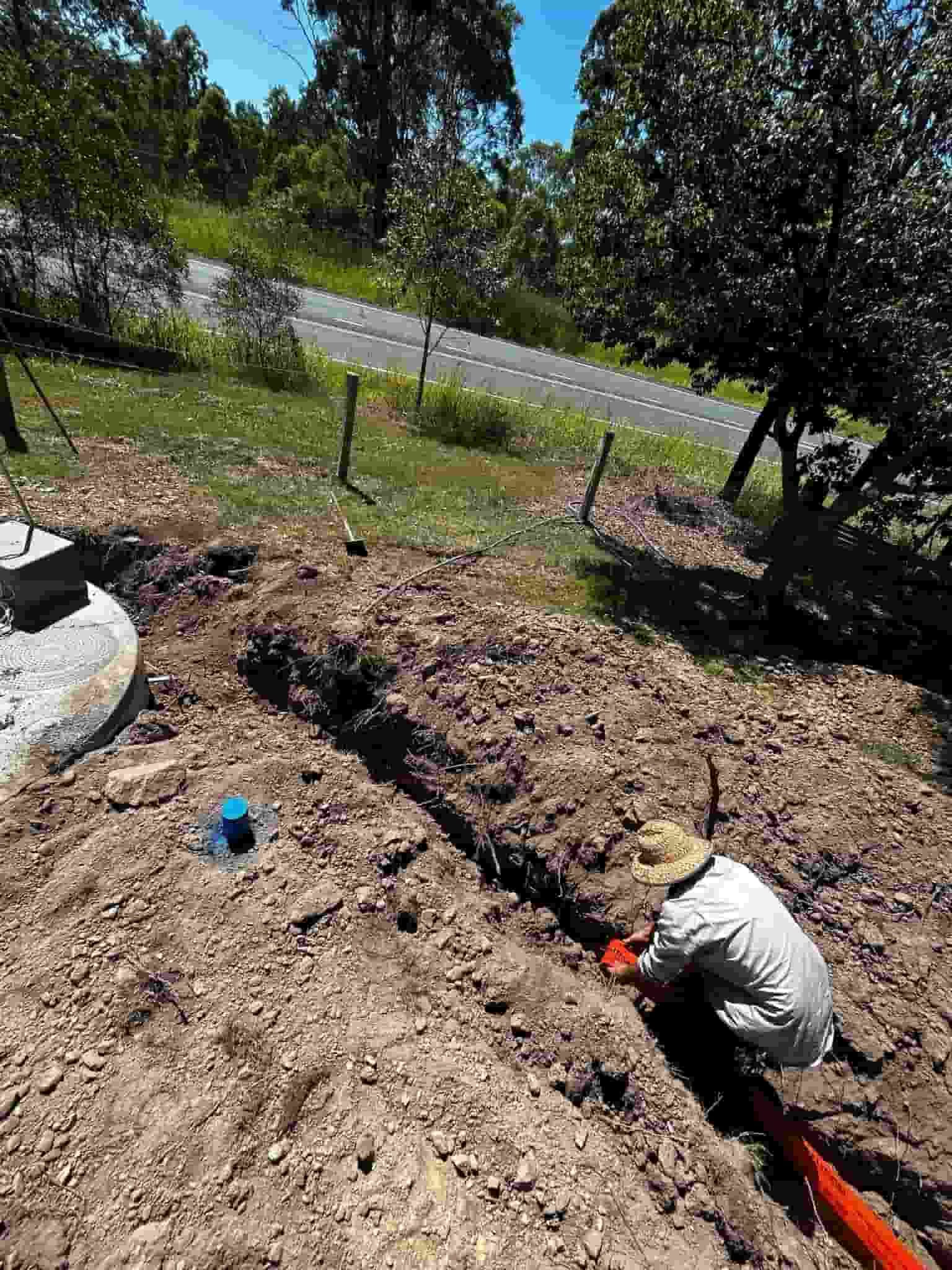 A man in a hat is kneeling in the dirt next to a pipe — Matt King Plumbing & Septic Systems in Taree, NSW