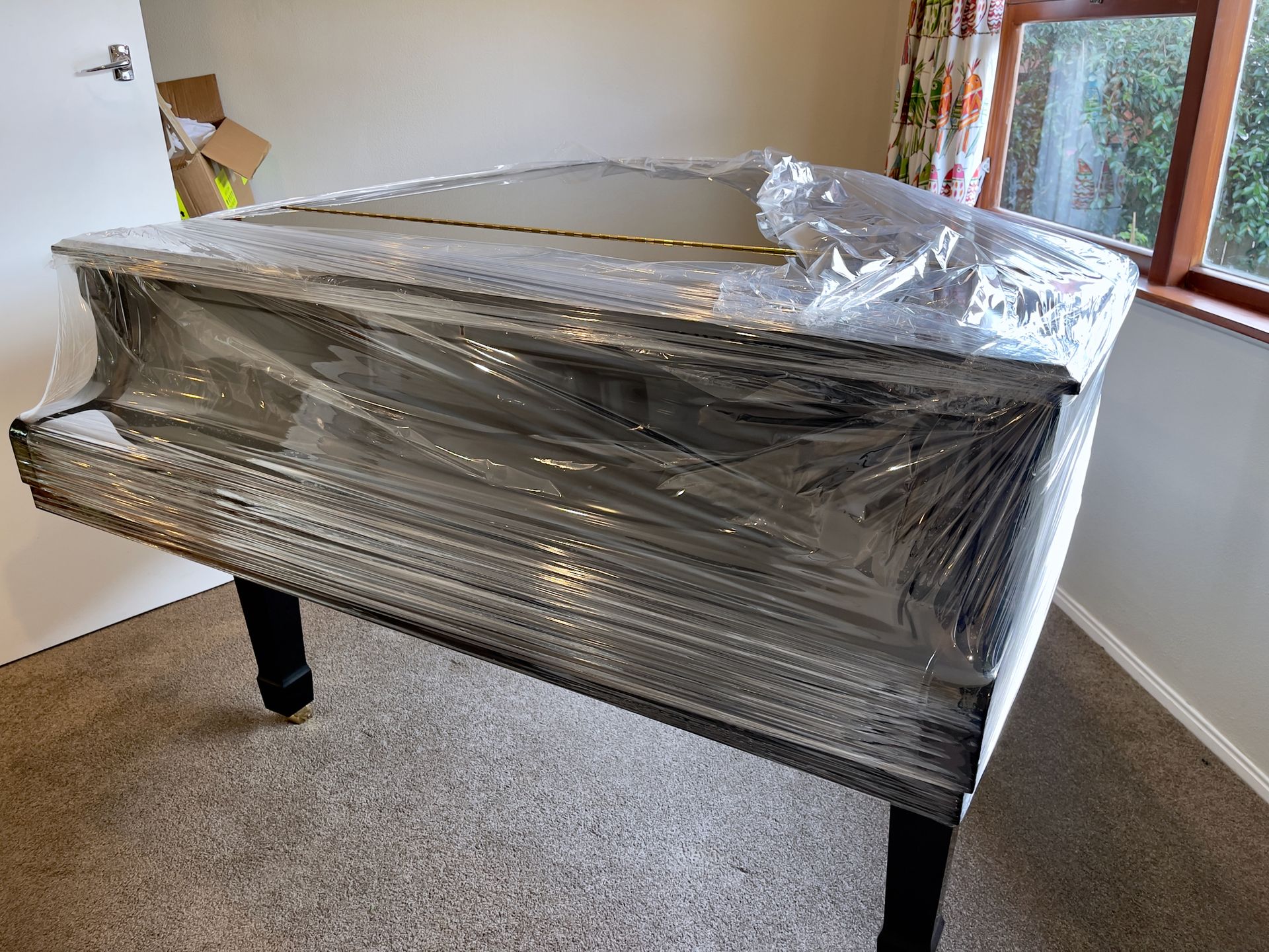 Glossy black grand piano partially covered in plastic wrap in preparation for removal.