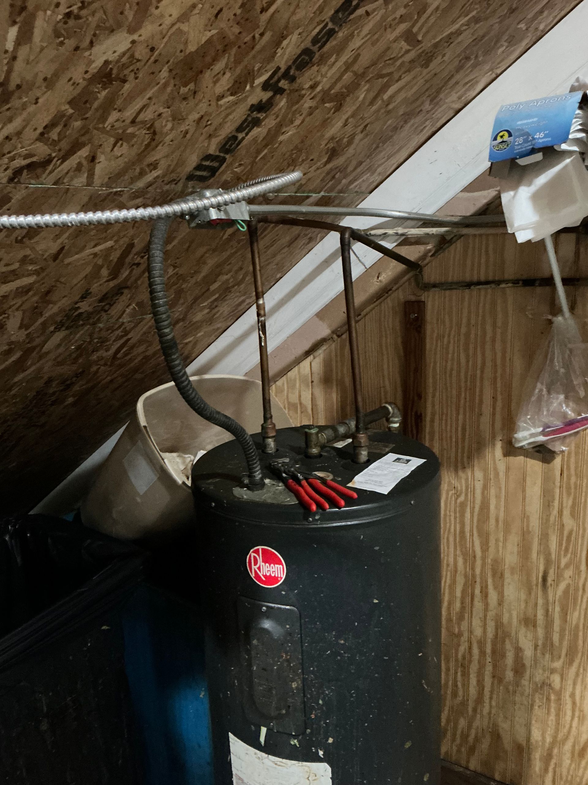 Black water heater in an attic, with copper pipes and electrical conduit above it.