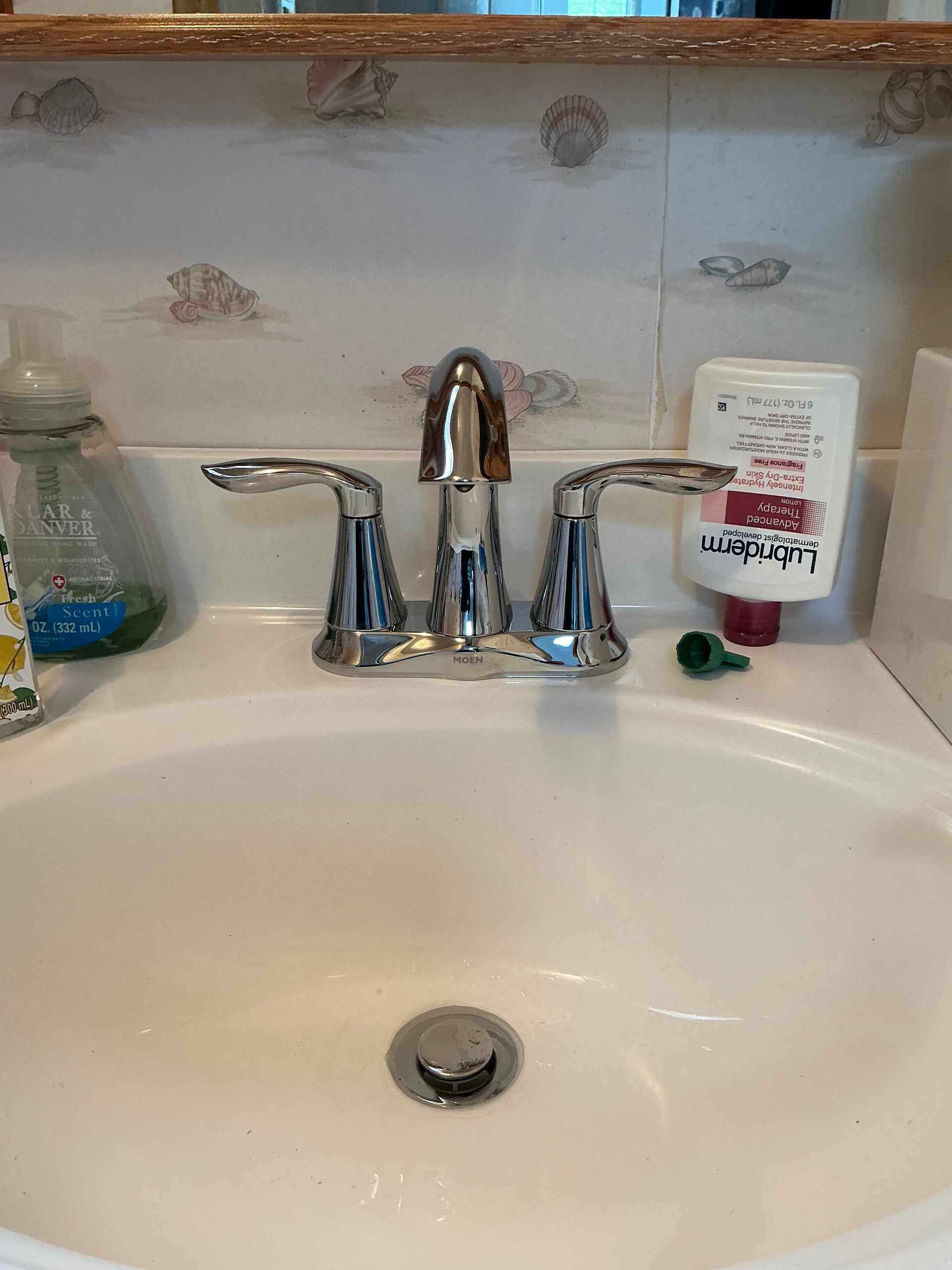 Bathroom sink with chrome faucet, soap dispenser, lotion, and floral patterned wall.