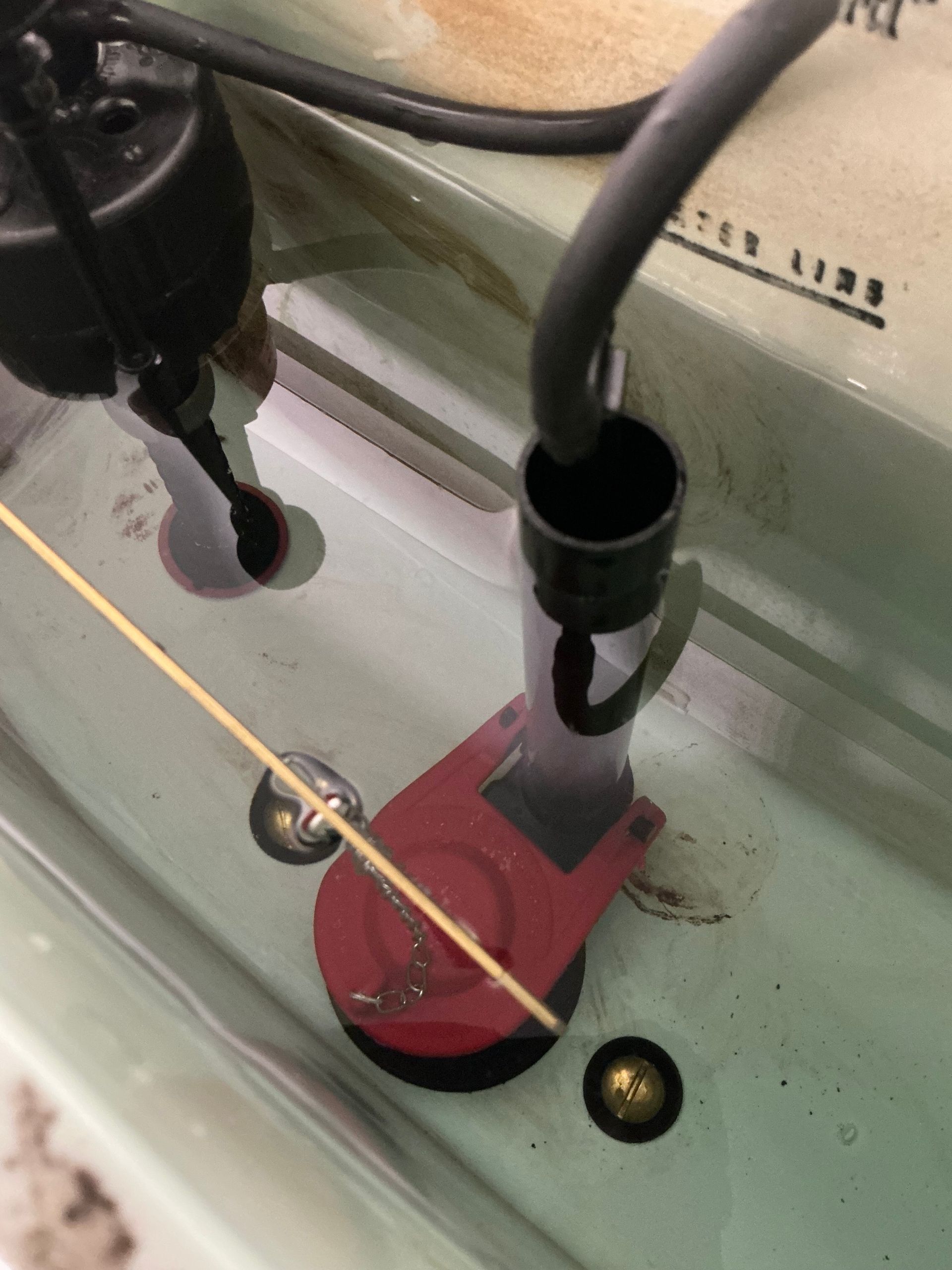 Toilet tank with red flapper, black fill valve, and floating arm.