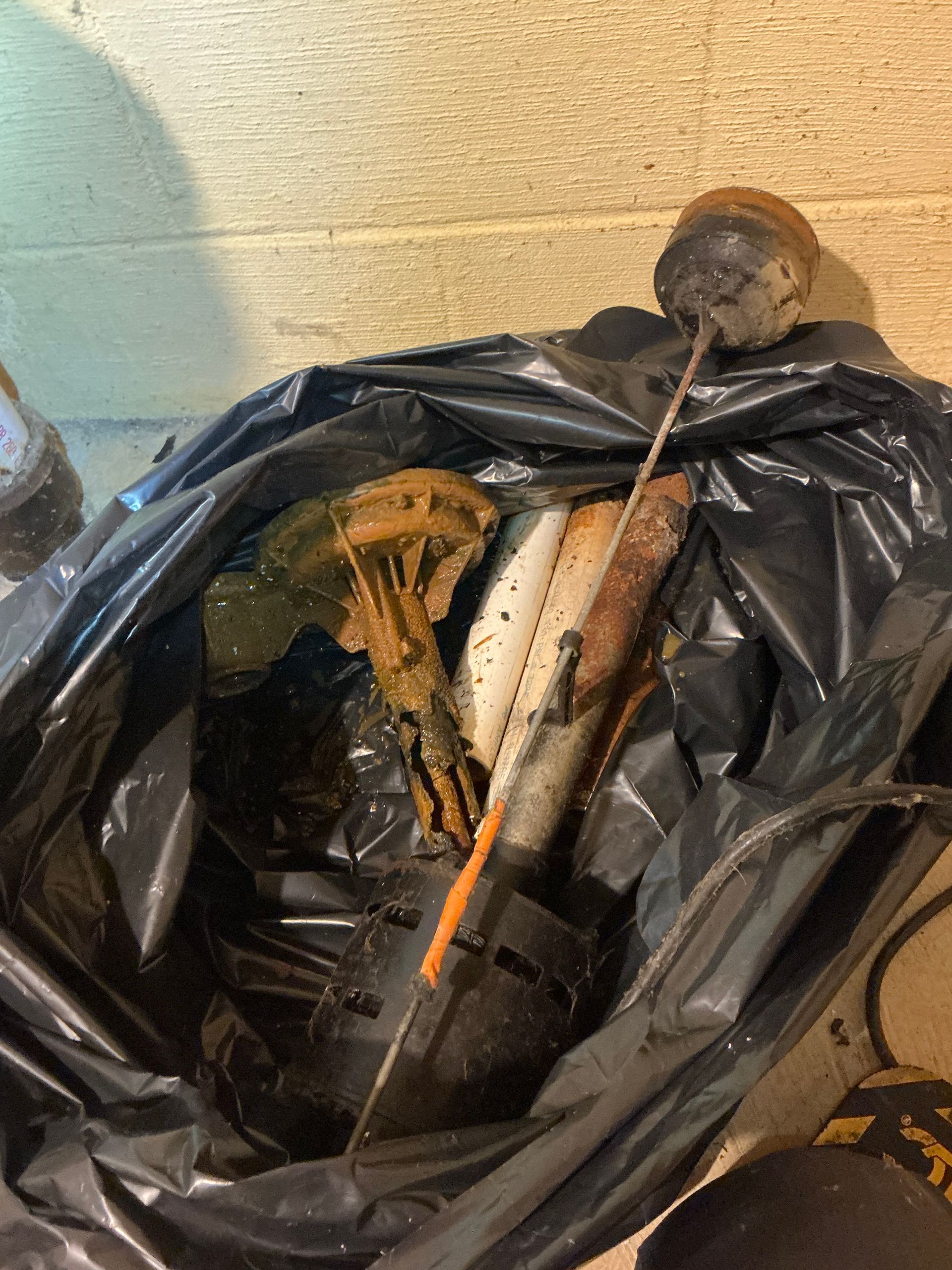 Black trash bag filled with rusty metal objects and debris, likely trash in a basement.