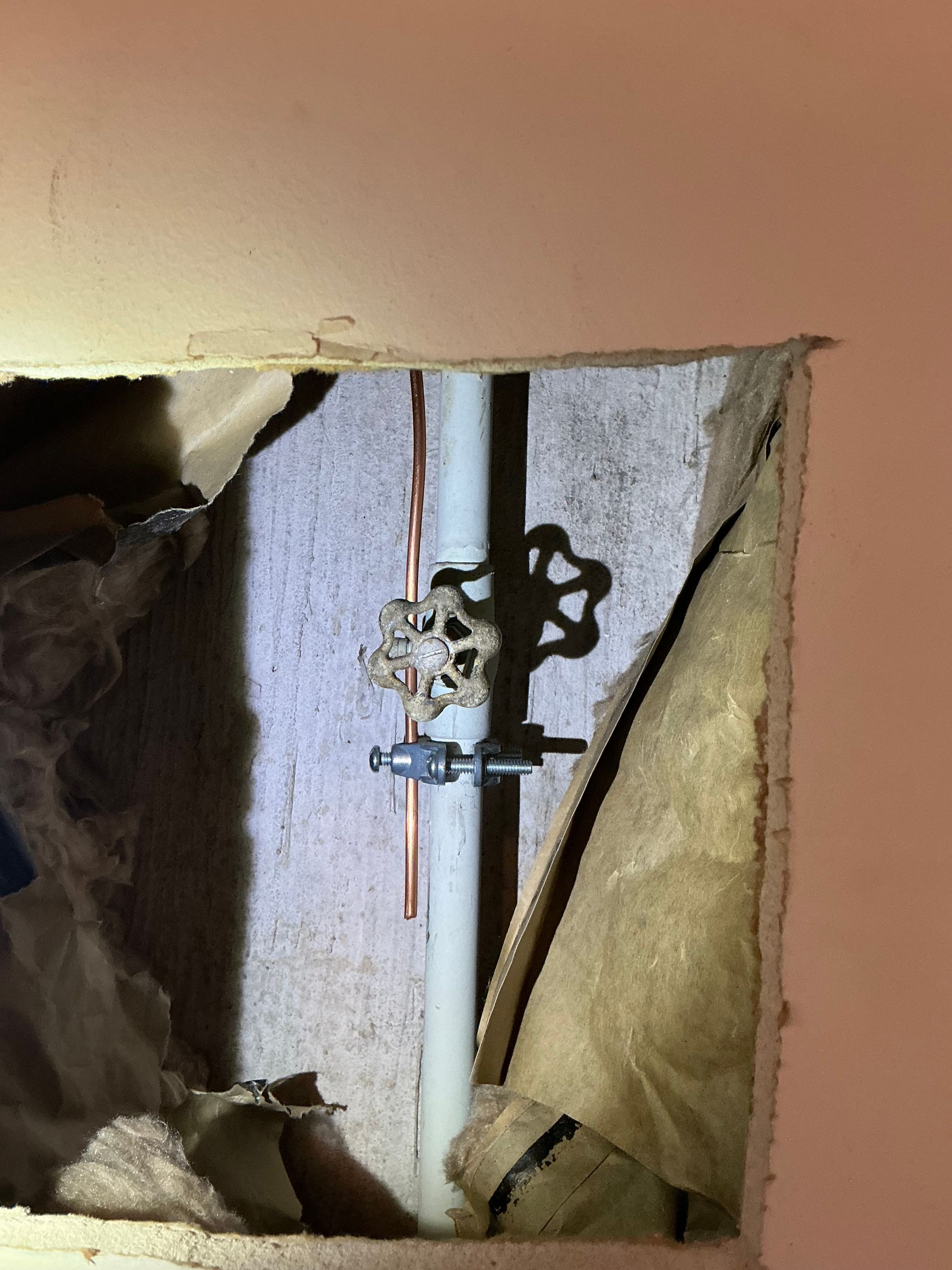 Copper pipe with water shut-off valve inside a wall opening; exposed insulation and drywall.