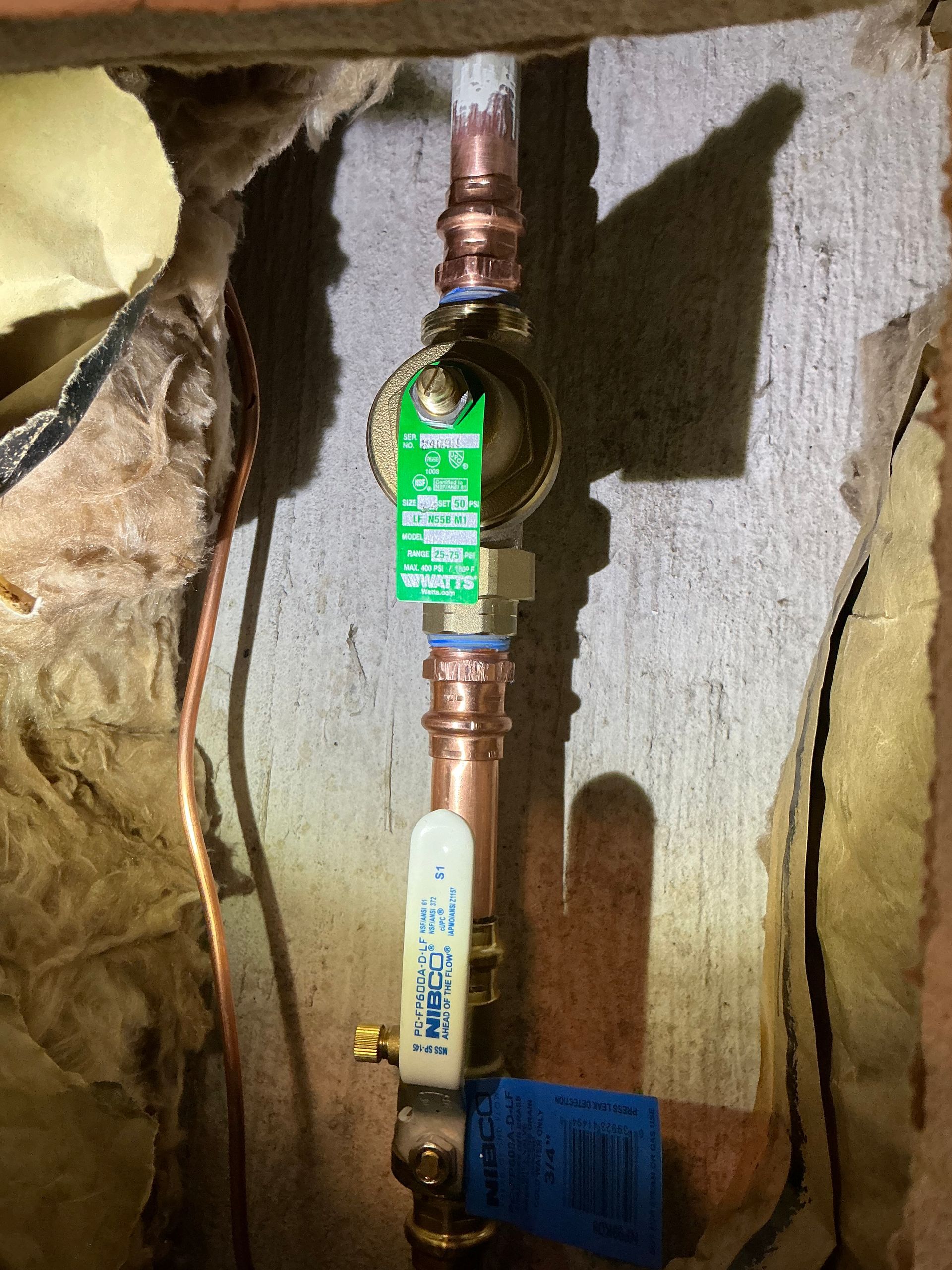 Copper pipes with a water pressure regulator and shutoff valve, mounted in a wall cavity.