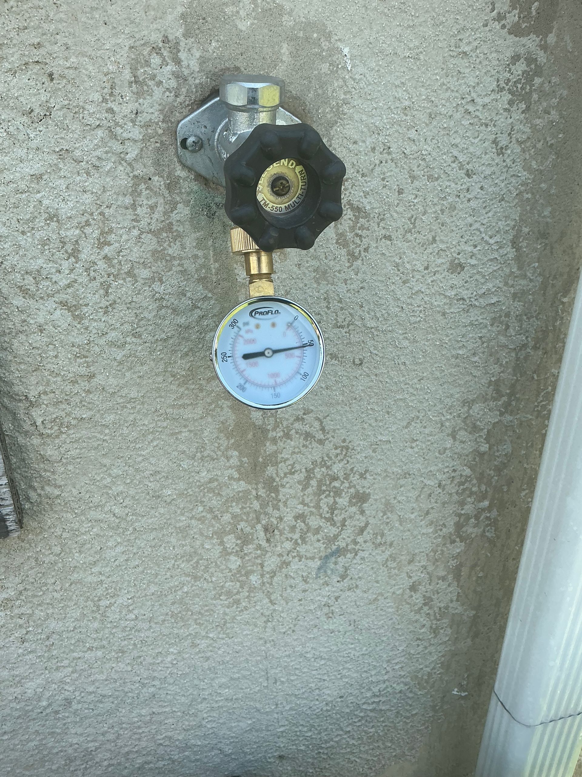 Water pressure gauge and valve attached to a concrete wall.