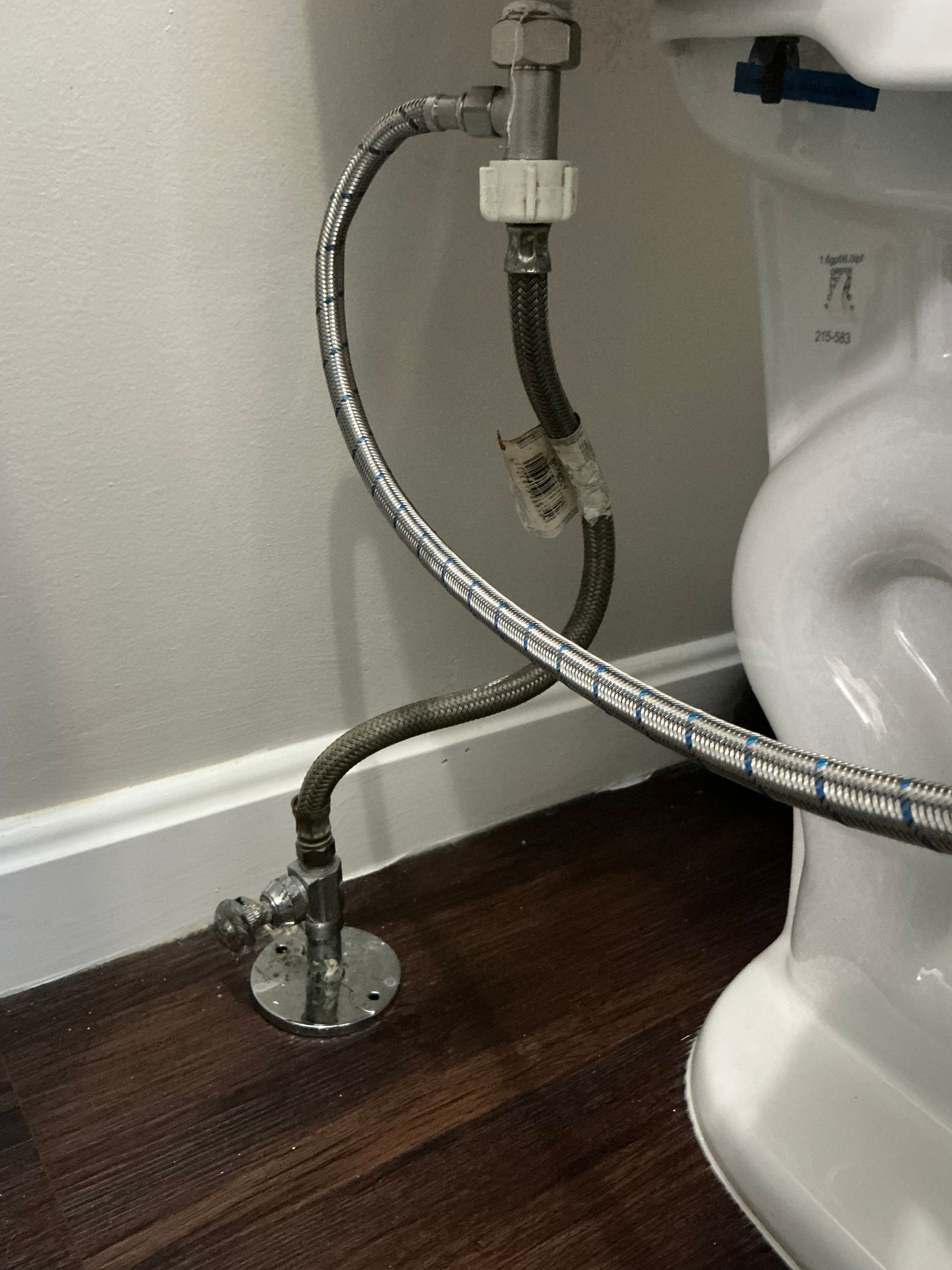 A toilet's water supply line connects from the wall to the toilet tank, with a shut-off valve at the floor.