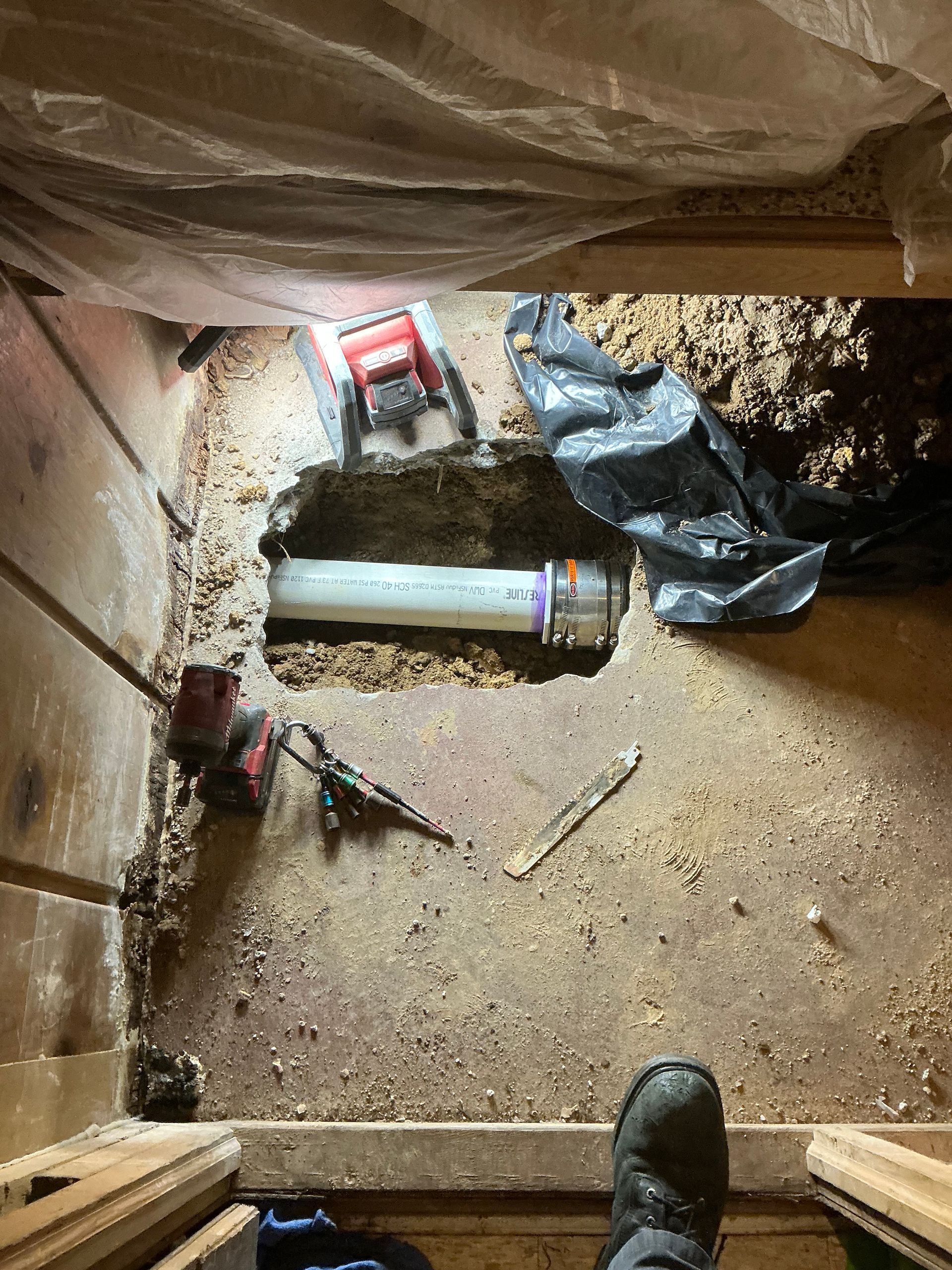 Plumbing pipe repair in a crawl space; tools and debris surround the white pipe.