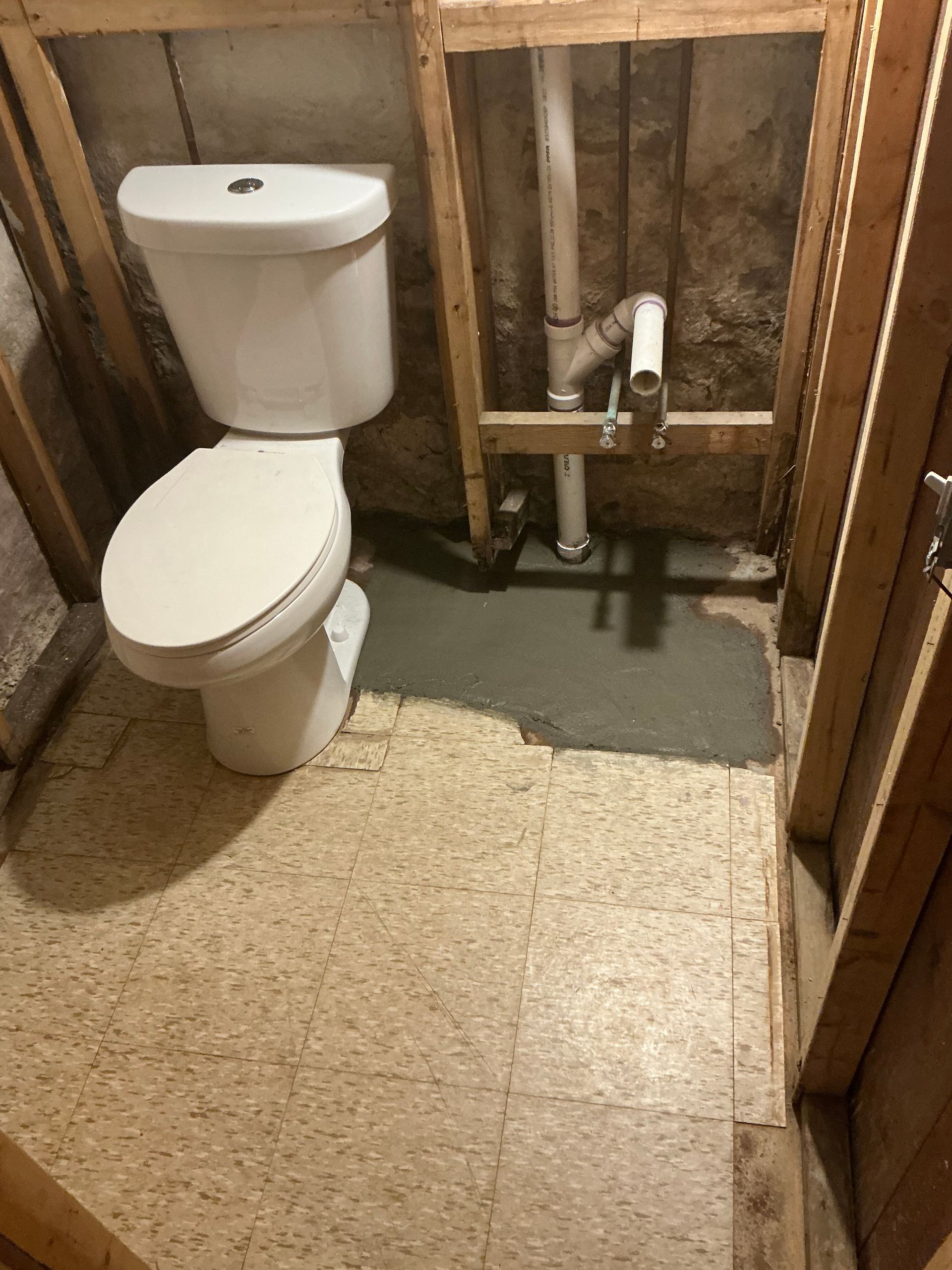 Toilet installed in a partially framed bathroom with a concrete floor patch.
