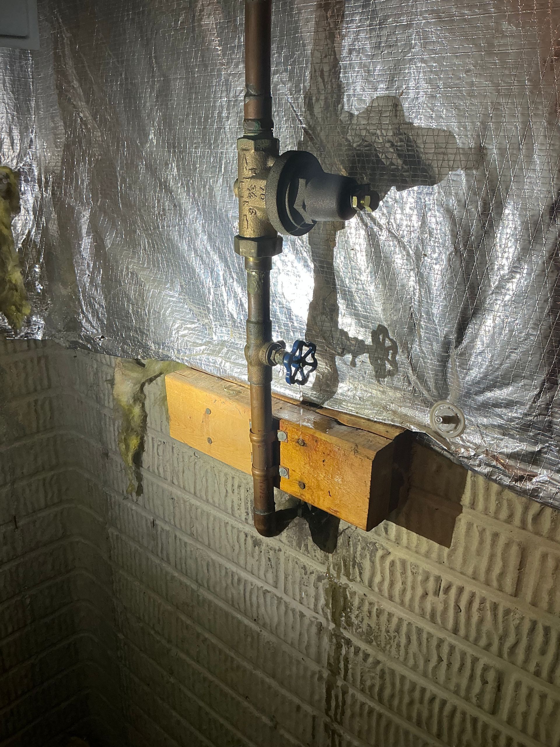 Copper pipes with valves and pressure regulator mounted on a brick wall, with wood support.