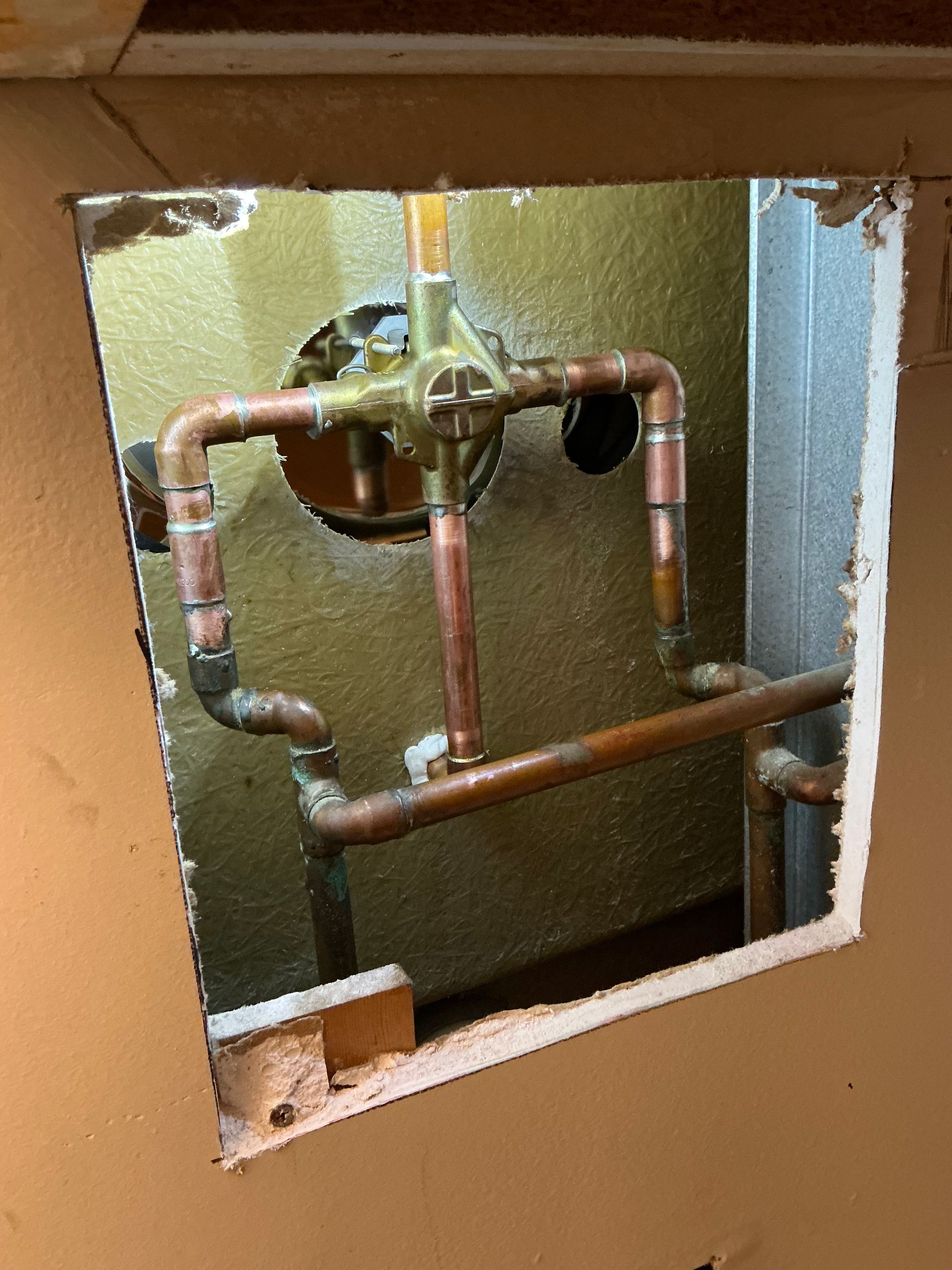 Copper plumbing pipes and a valve inside a wall opening.
