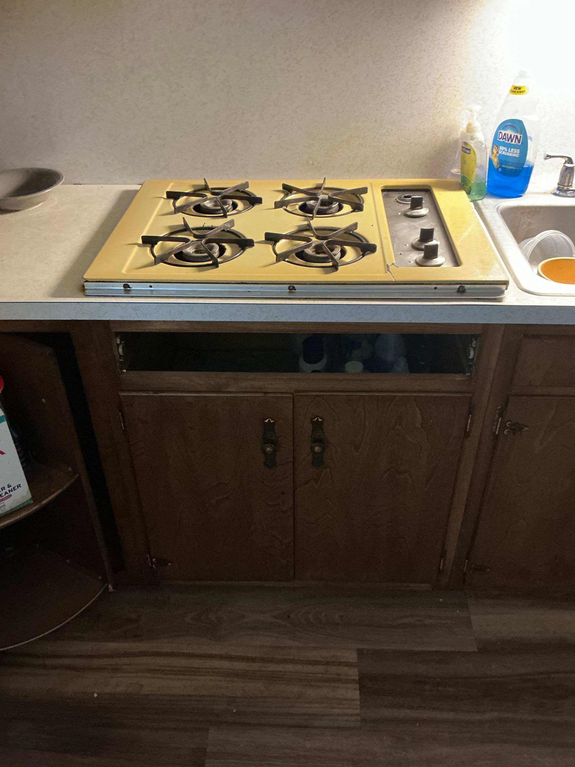 Gas stove with four burners set in a countertop above wooden cabinets and a sink.
