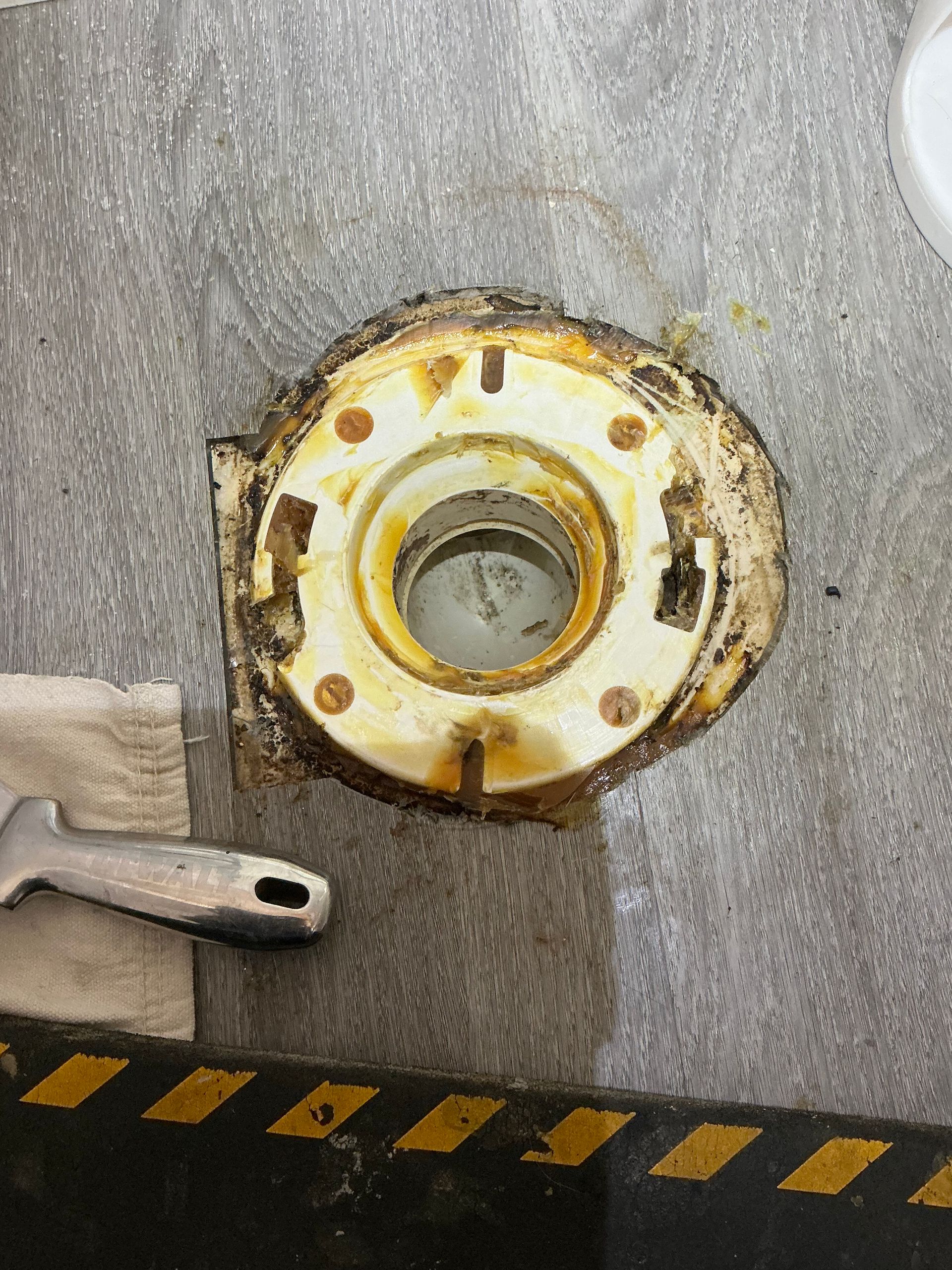 Toilet flange, rusty with bolts, on a dirty floor, with a wrench.