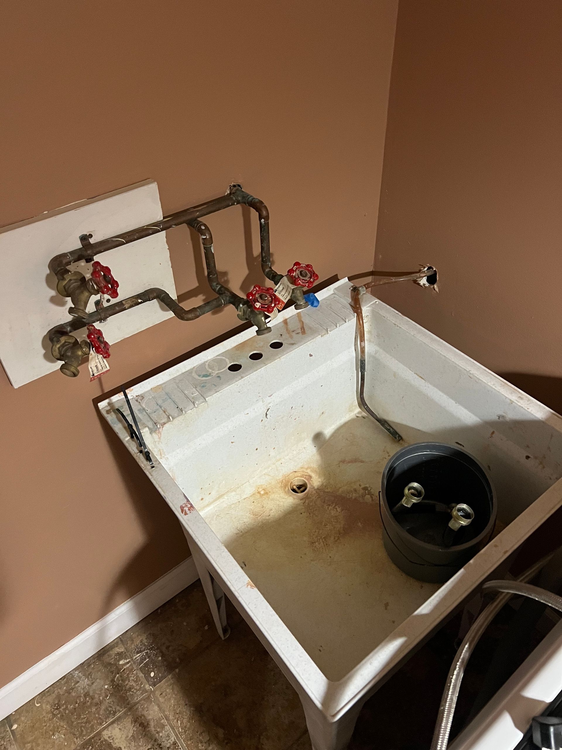 Laundry room sink with exposed copper plumbing and red and blue valves. Dirty sink basin.