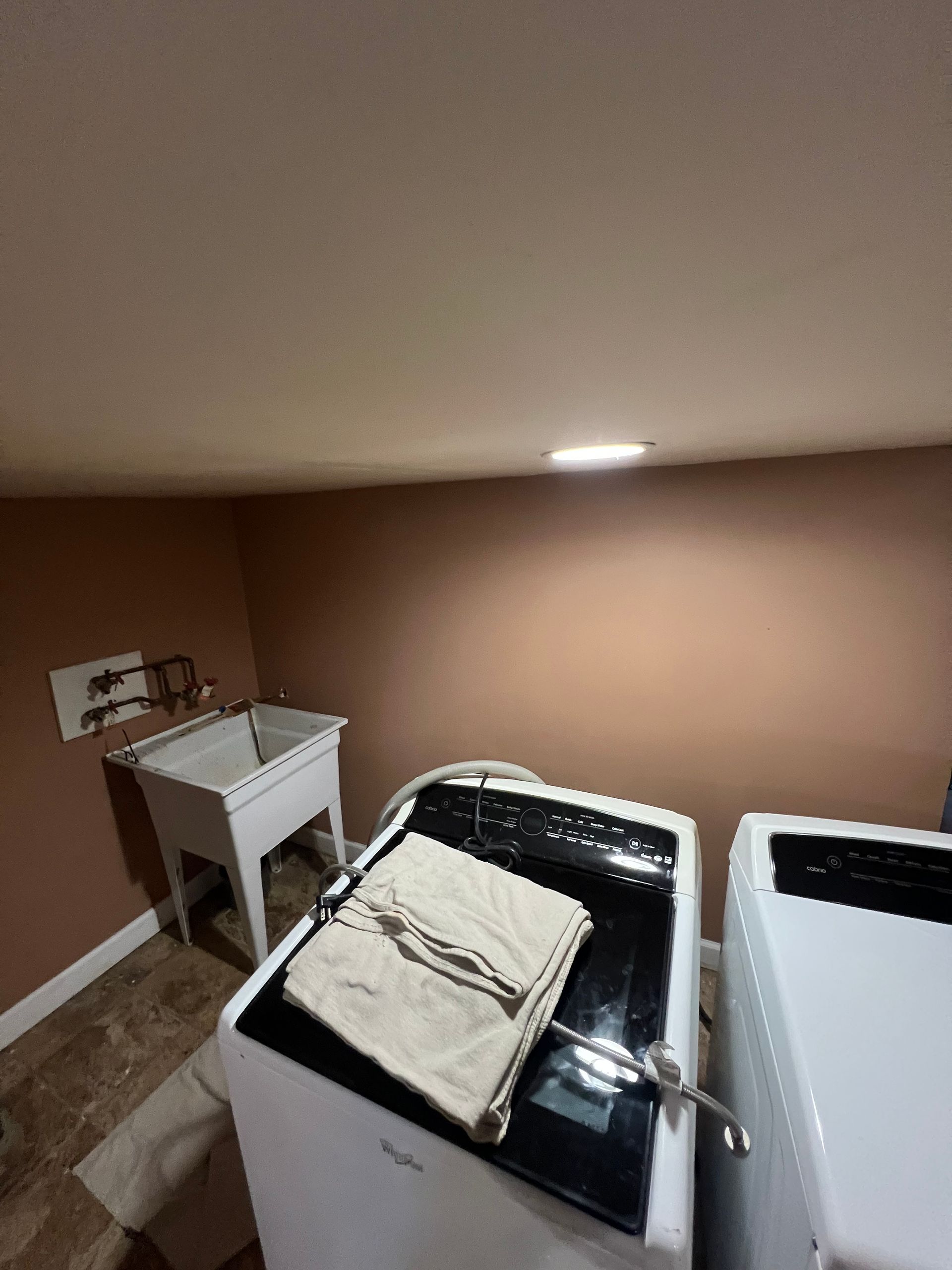 Laundry room with white appliances, washbasin, and brown walls. A towel rests on a washing machine.