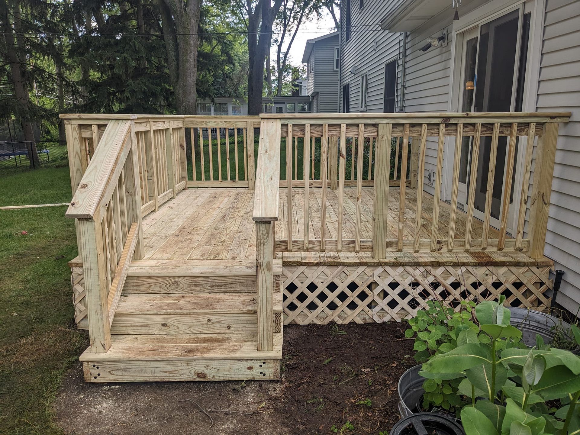 A wooden deck with stairs leading up to it is in the backyard of a house.