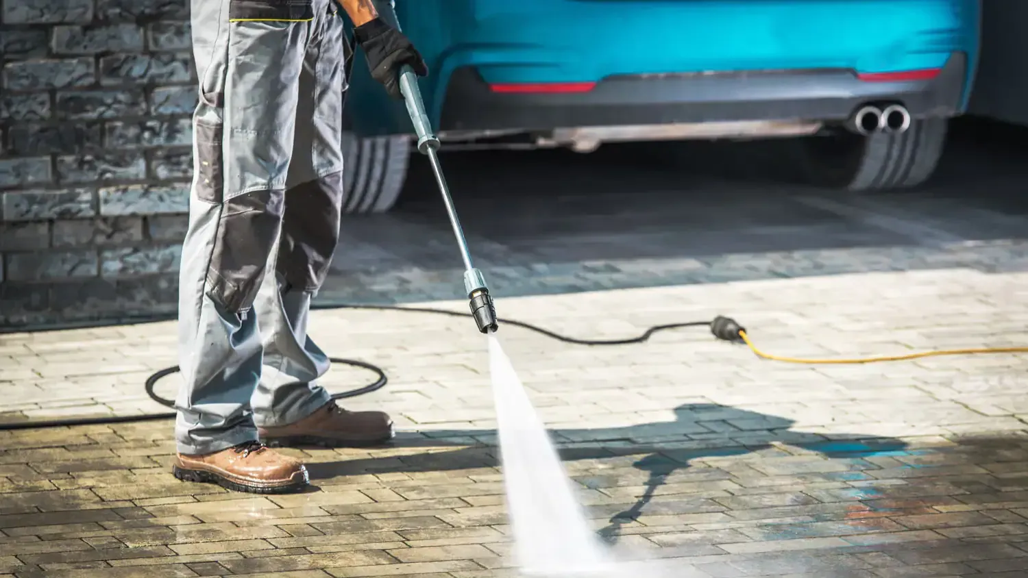 A man is using a high pressure washer to clean a driveway.