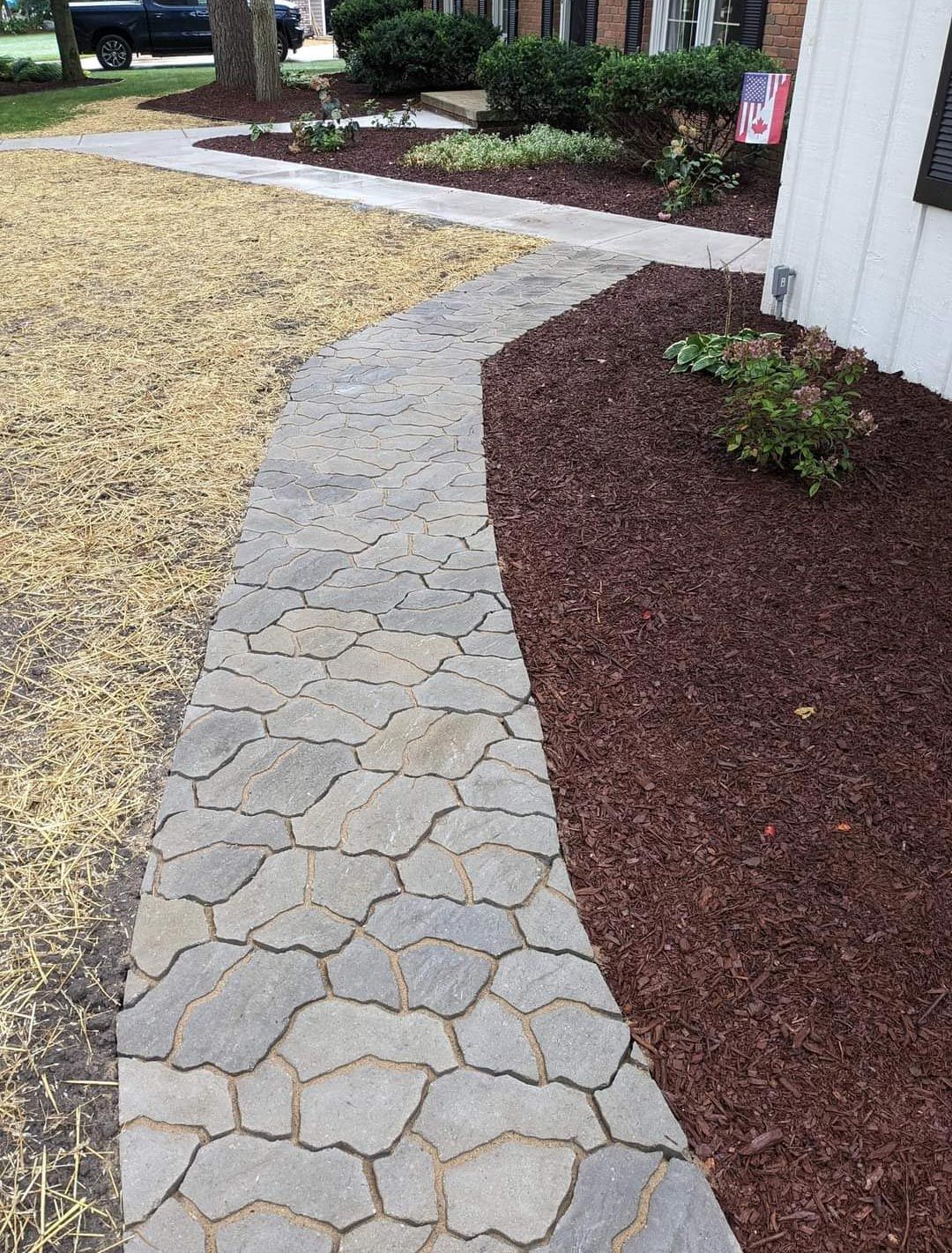 A stone walkway leading to a house next to a pile of mulch.
