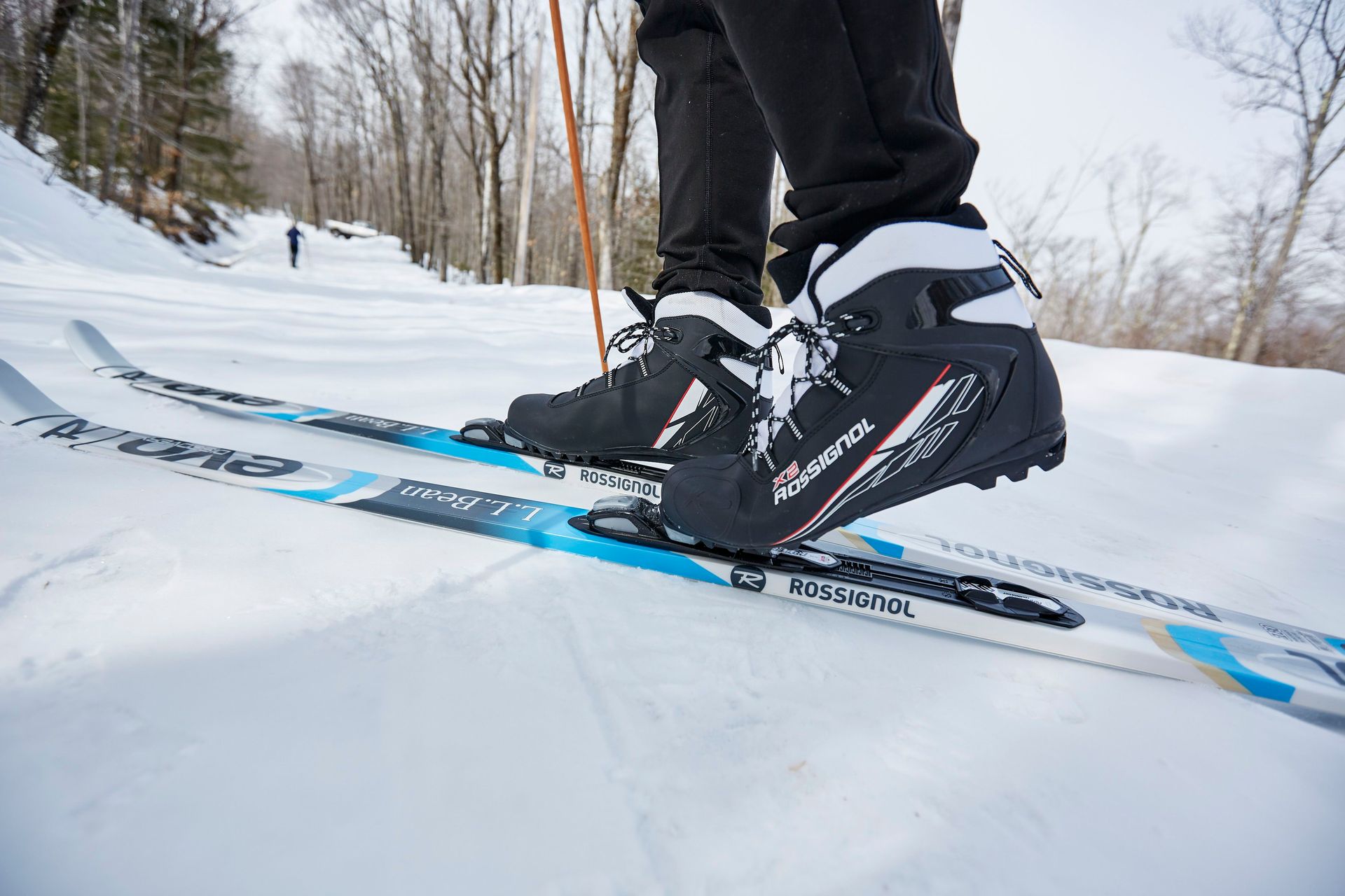 Close-up picture of a person's cross-country ski boots, while they are standing on skis on a trail.