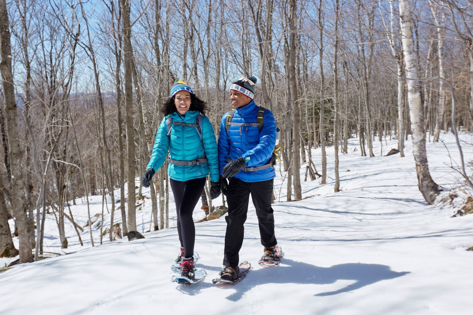 A man and a woman snowshoeing on a forest trail.