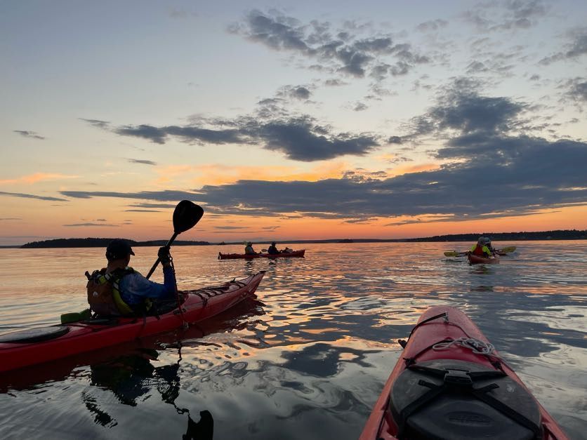 Group of kayakers on the ocean at sunset.