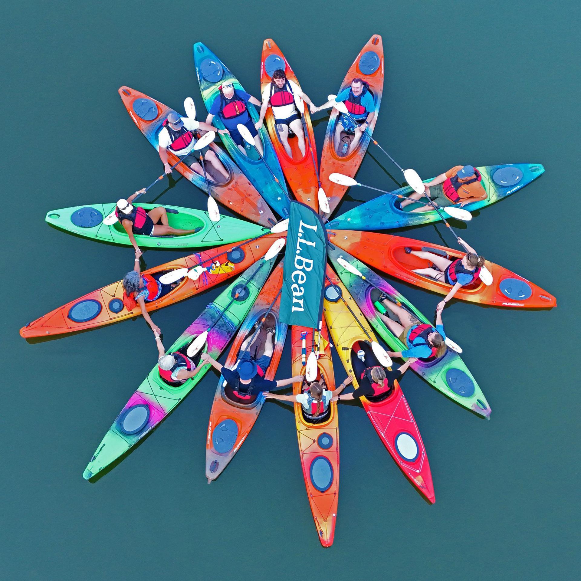 group of kayakers on a lake, forming a pinwheel.