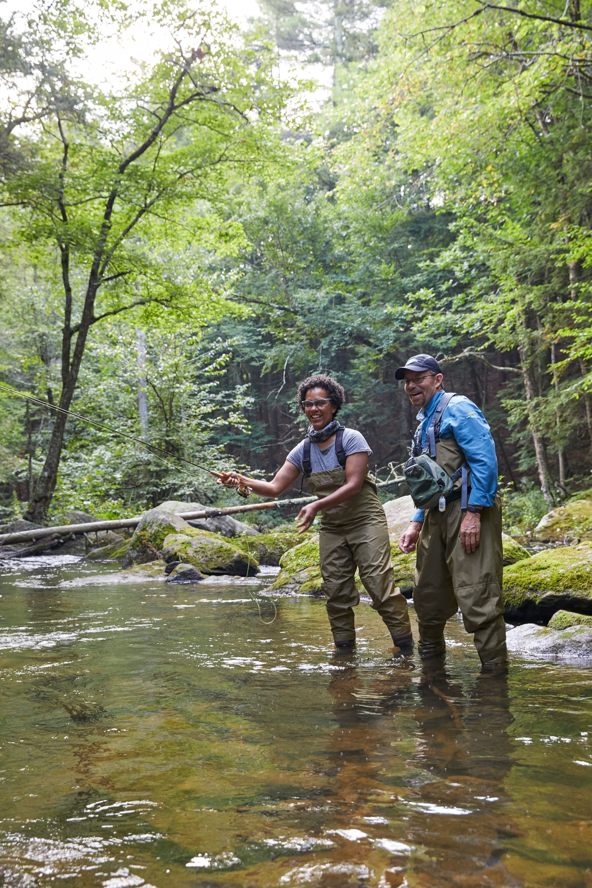 Woman standing in a stream fly fishing, with her guide looking on.