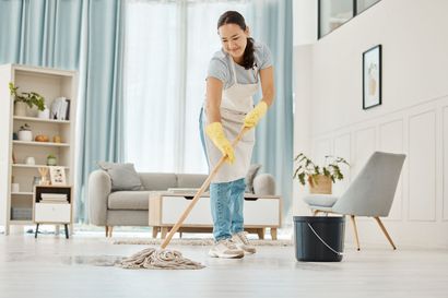 Woman wearing apron and gloves mops a bright, clean living room.