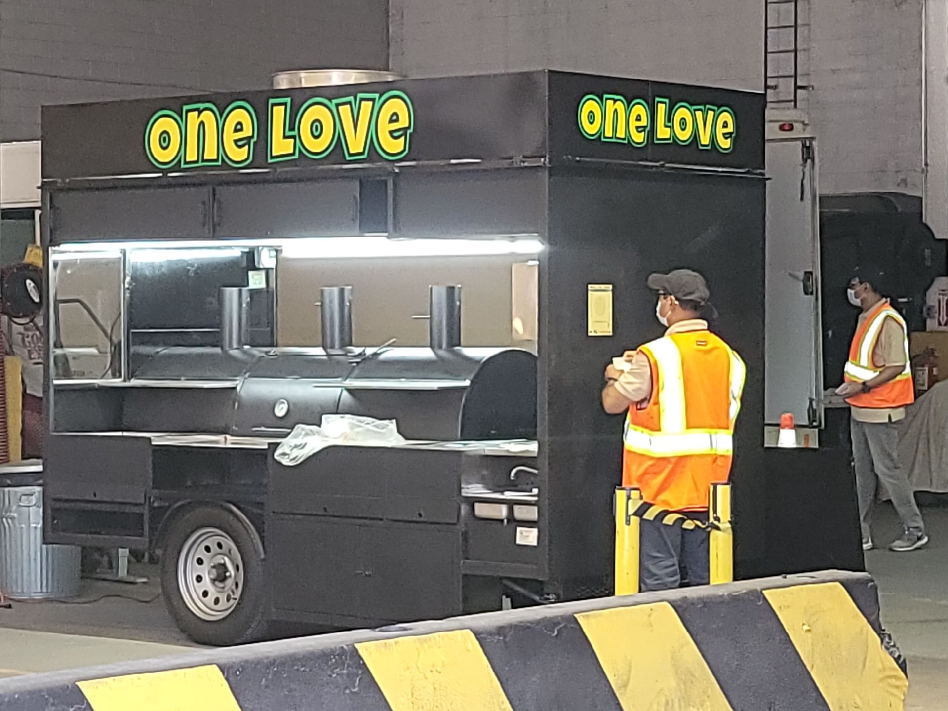 A man in an orange vest is standing in front of a one love food truck.