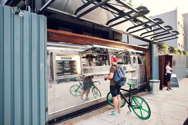 A man is standing on the sidewalk with a bicycle in front of a food truck.