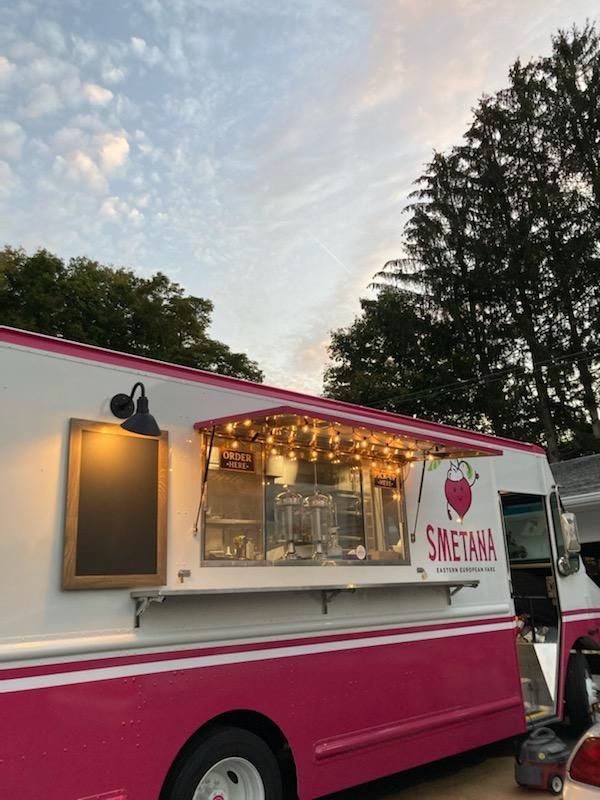 A pink and white food truck is parked in a parking lot.