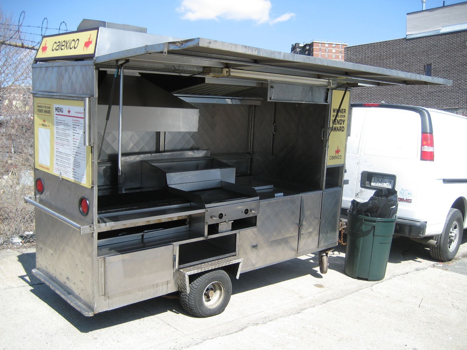 A food truck is parked next to a white van
