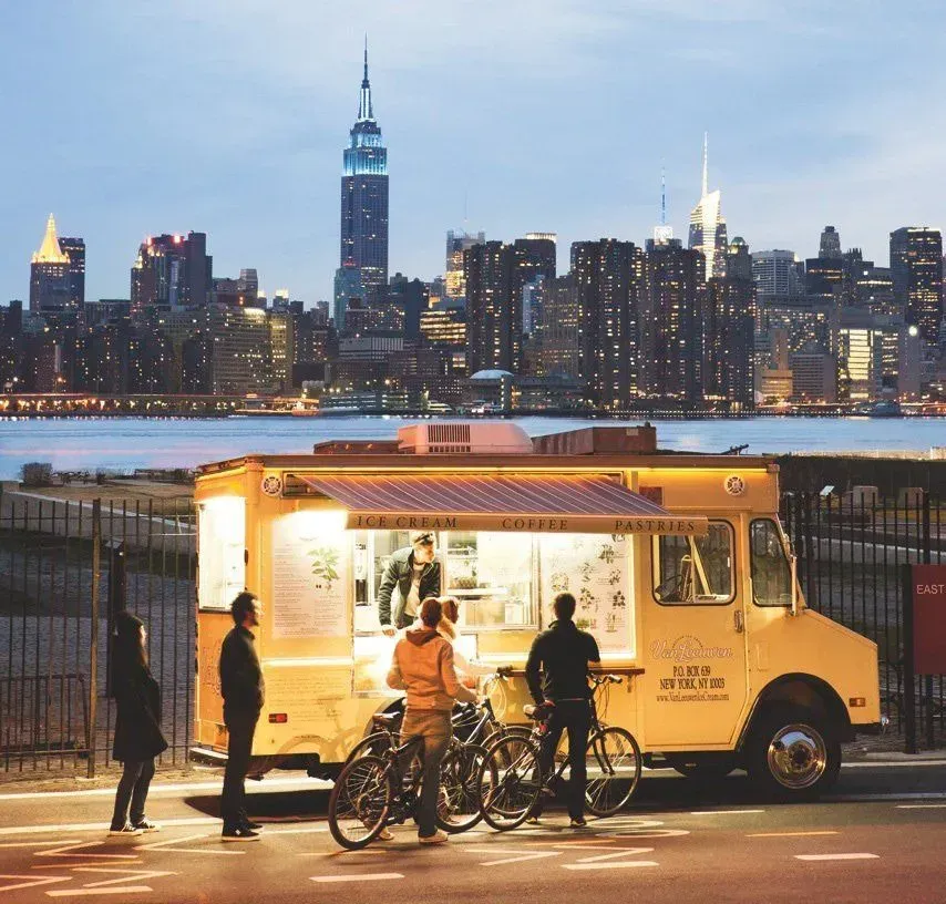 Image of a yellow food truck parked in front of the New York City skyline