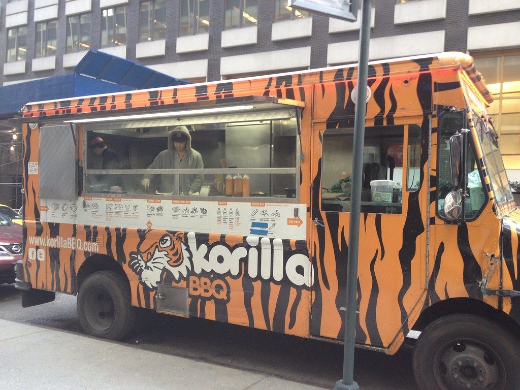 A food truck is parked on the side of the road in front of a building.