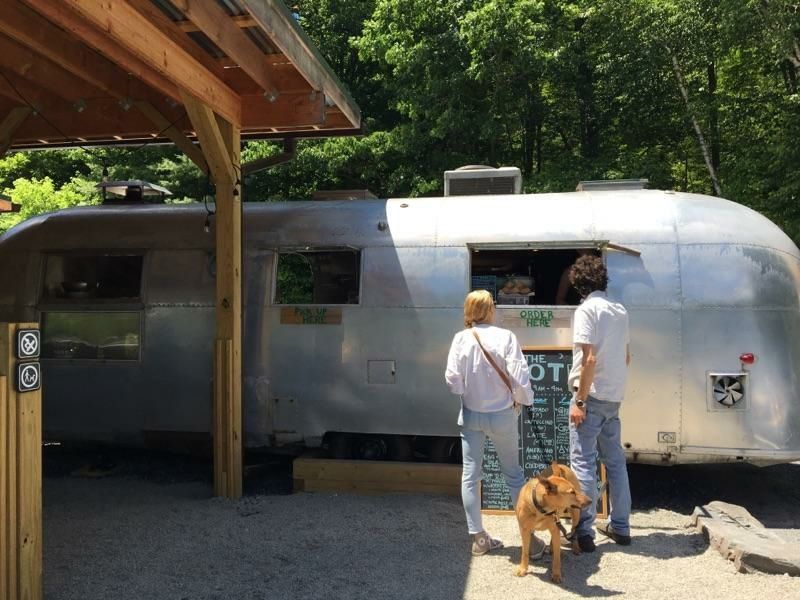 A couple and a dog are standing in front of an airstream trailer.