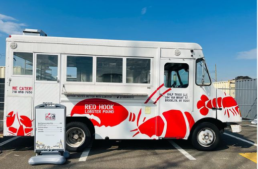 A red hook food truck is parked in a parking lot