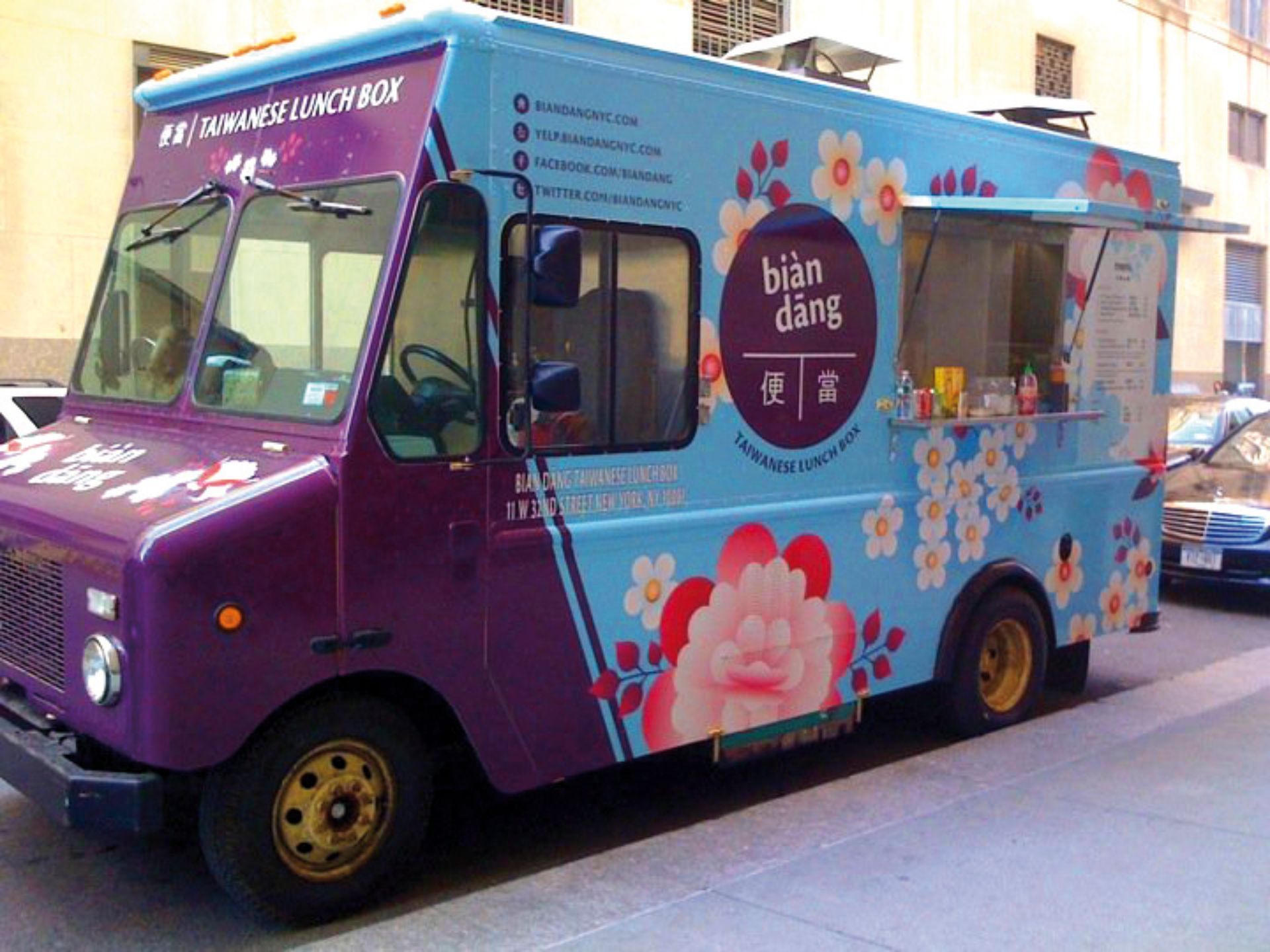 A purple and blue food truck is parked on the side of the road