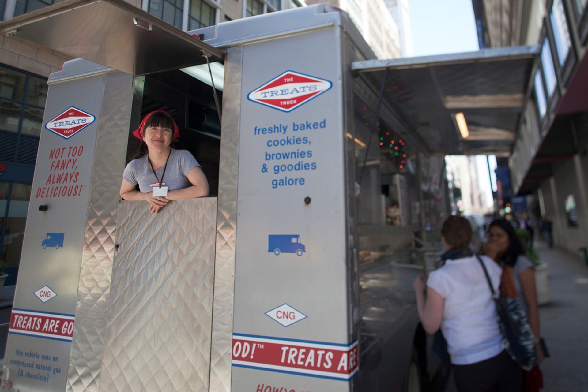 A woman stands in front of a food truck that says treats