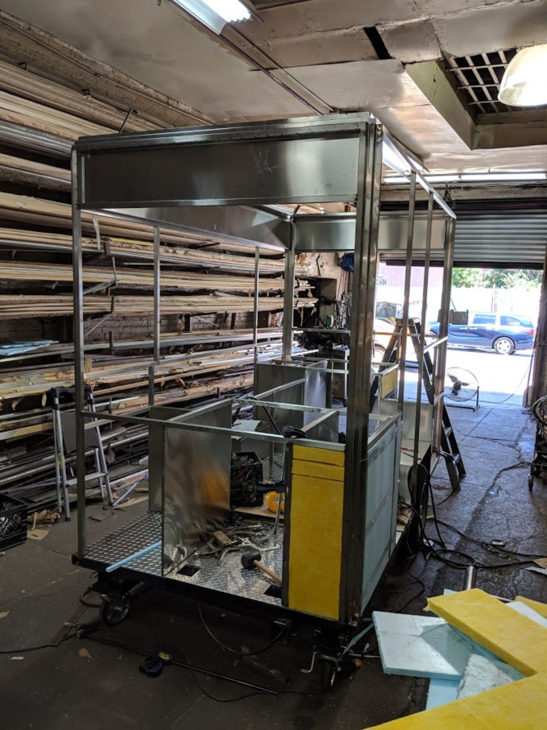 A stainless steel food cart is being built in a garage.