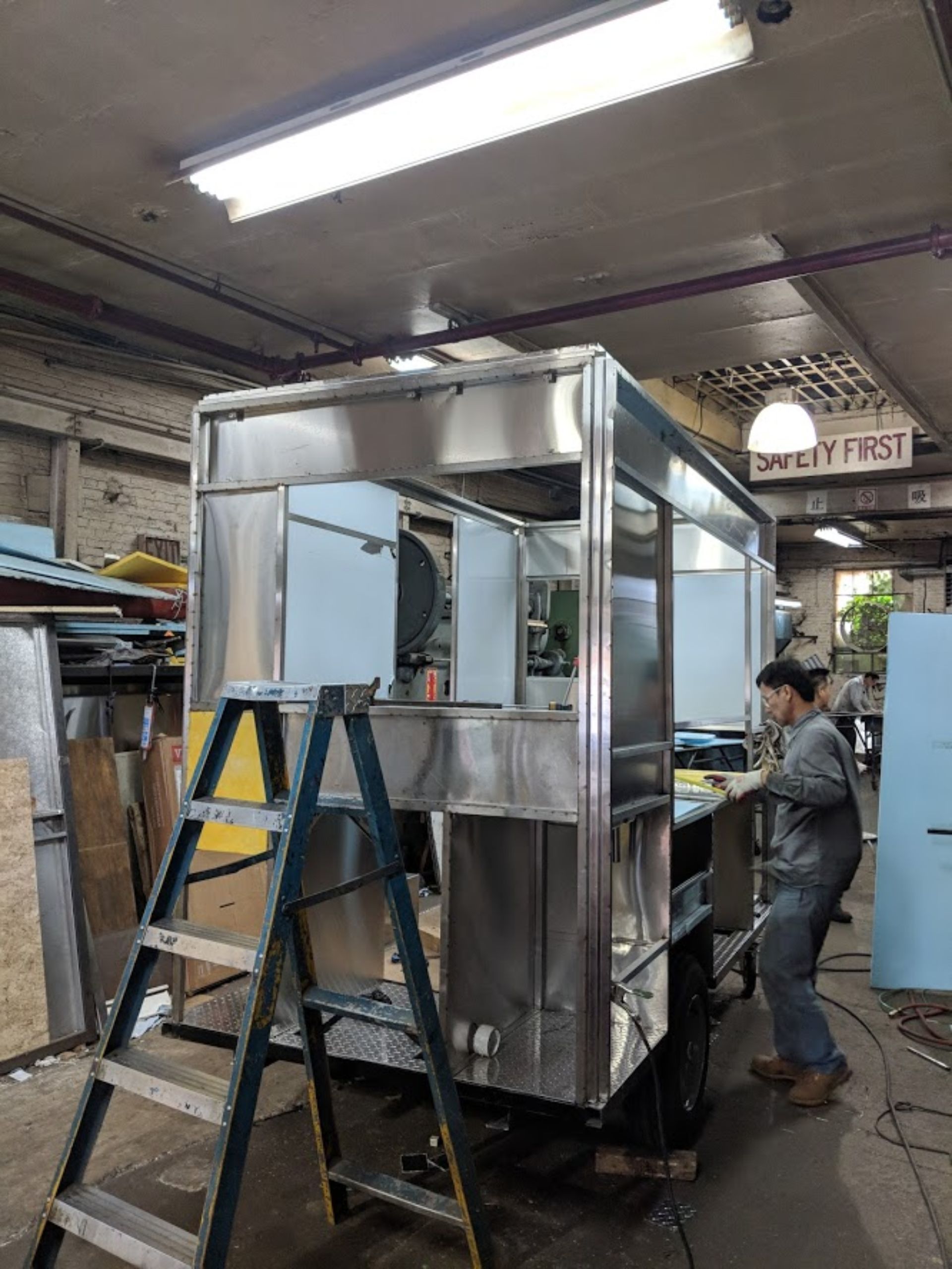 A man is working on a stainless steel food truck in a factory.