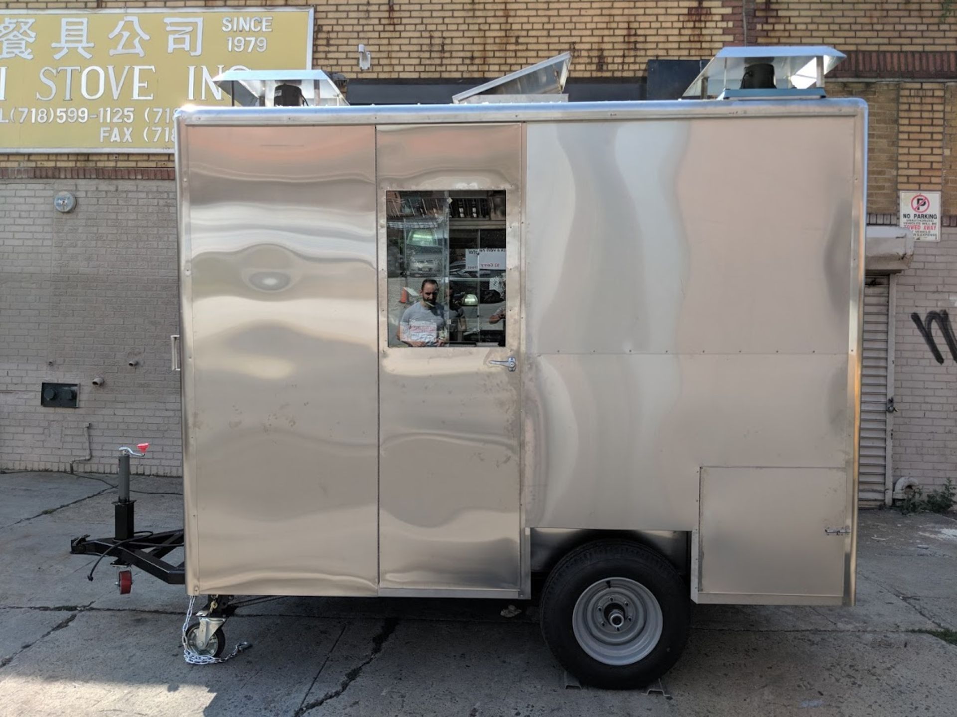 A stainless steel trailer is parked in front of a brick building.