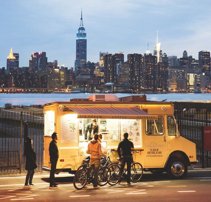 A yellow food truck is parked in front of a city skyline