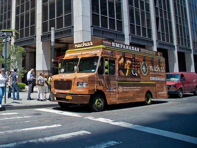 A food truck is parked on the side of the road in front of a building.