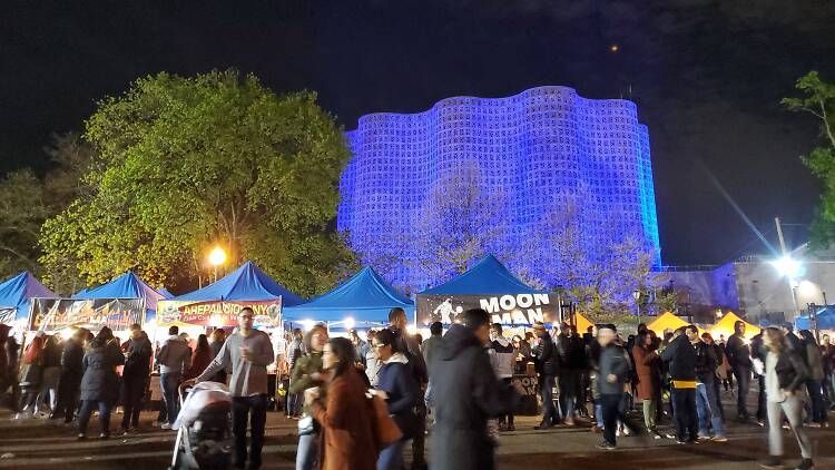 A group of people are standing in front of a building that is lit up at night.